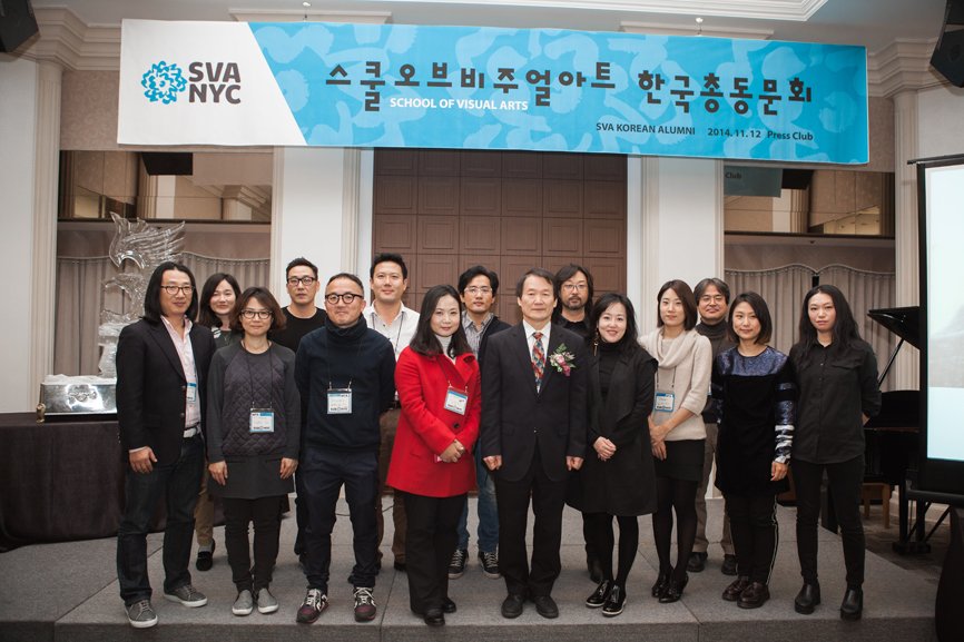A group photo of 15 individuals taken beneath the alumni gathering banner.