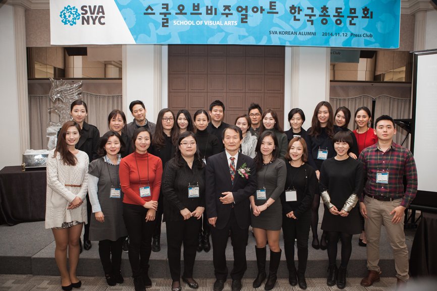 A group photo of 23 individuals taken beneath the alumni gathering banner.