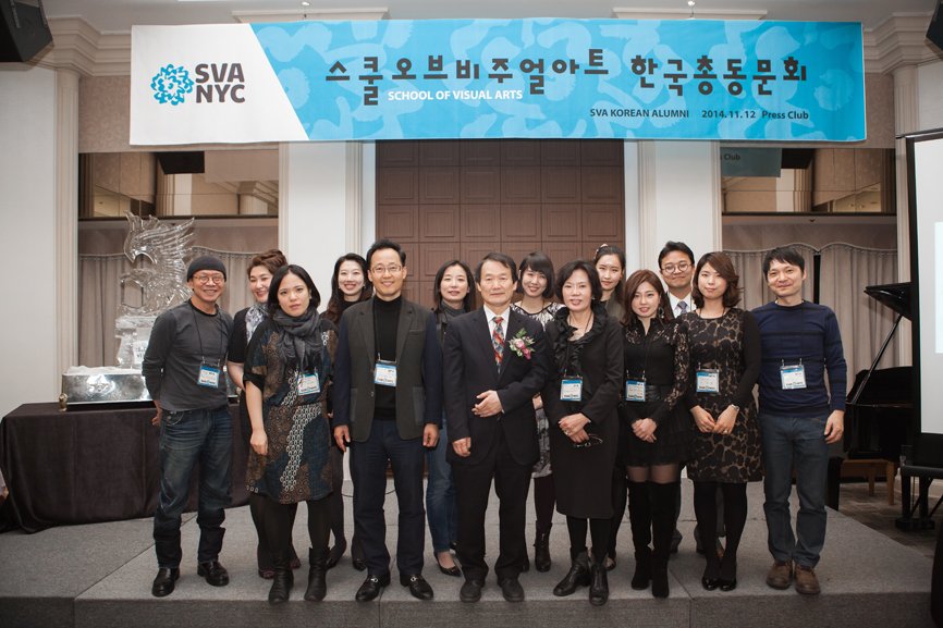 A group photo of 14 individuals taken beneath the alumni gathering banner.