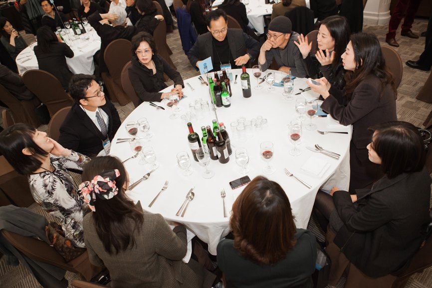 Eleven Fine Arts graduates are seated around a white round table, engaging in conversation.