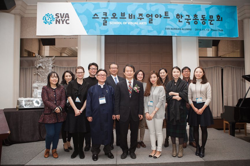 A group photo of 13 individuals taken beneath the alumni gathering banner.