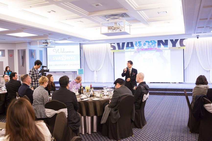 Among the alumni gathered around the round table, President Seo Myung-deok, the alumni association president, is standing at the front with a microphone, delivering a speech.
