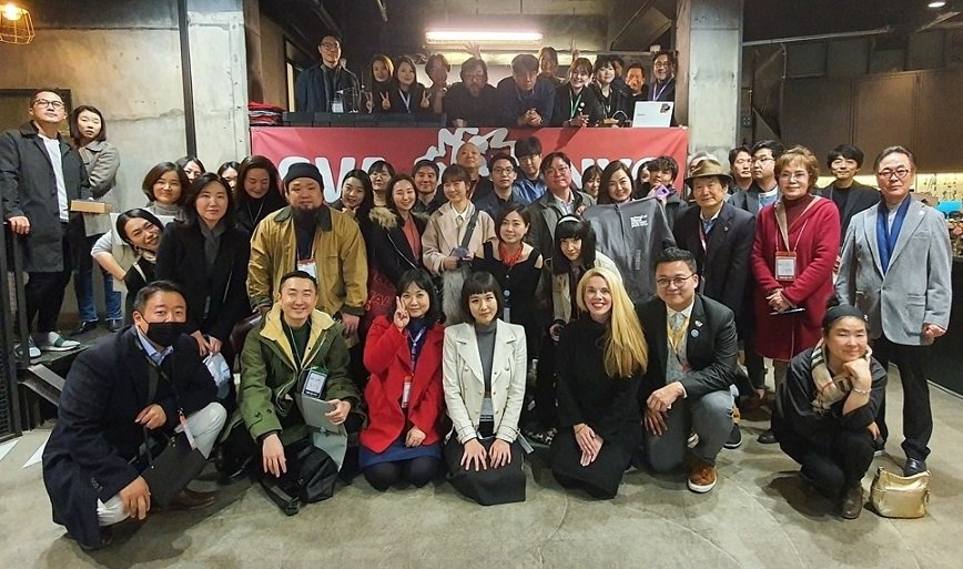 A group photo of approximately 45 graduates, divided into two rows on two levels, is being taken.