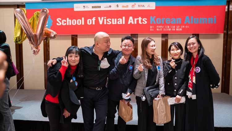 Six men and women are posing. There is a red banner in the background that reads "School of Visual Arts Korean Alumni."