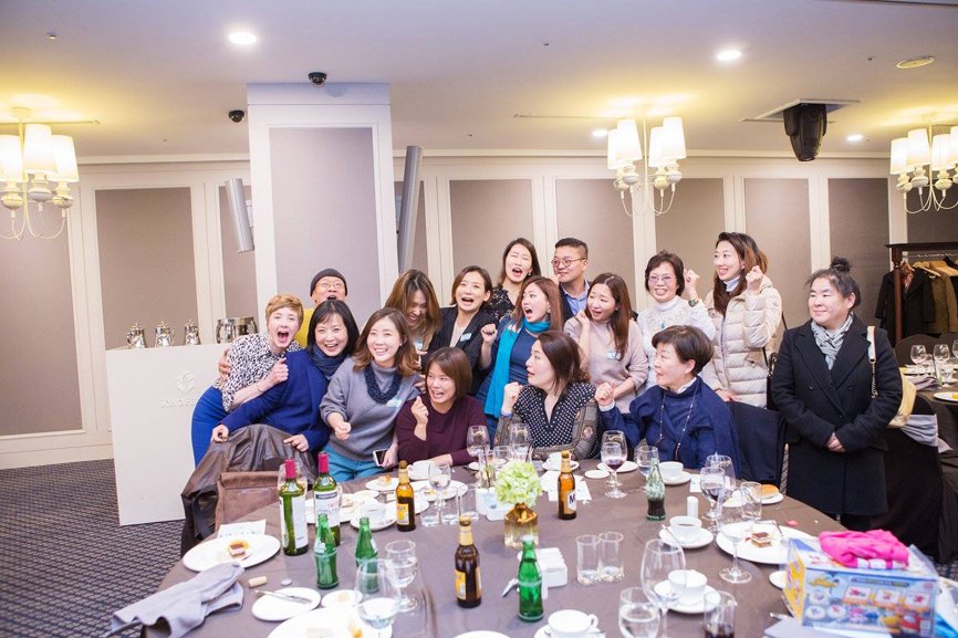Fifteen graduates and Alumni Affairs Director, Jane Nuzzo, are striking poses for a photo behind the round table.