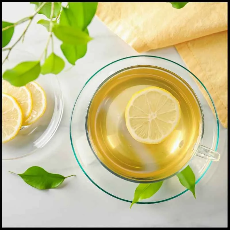 A cup of green tea with a lemon slice floating, plus a plate of lemon slices