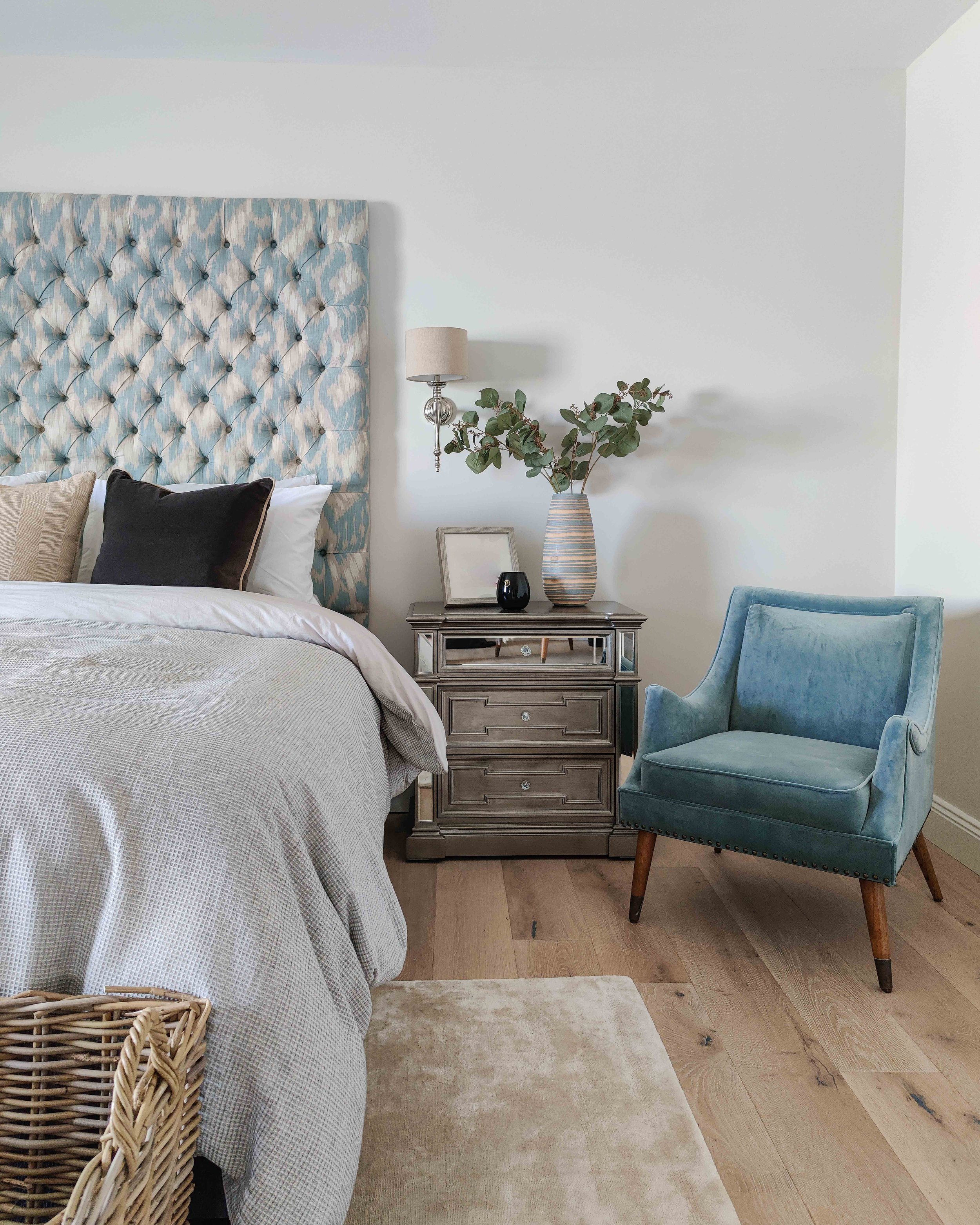 Luxury bespoke deep-button headboard in Zoffany fabric with mirrored bedside locker , chrome wall light and blue velvet chair - interior design by serpentine interiors