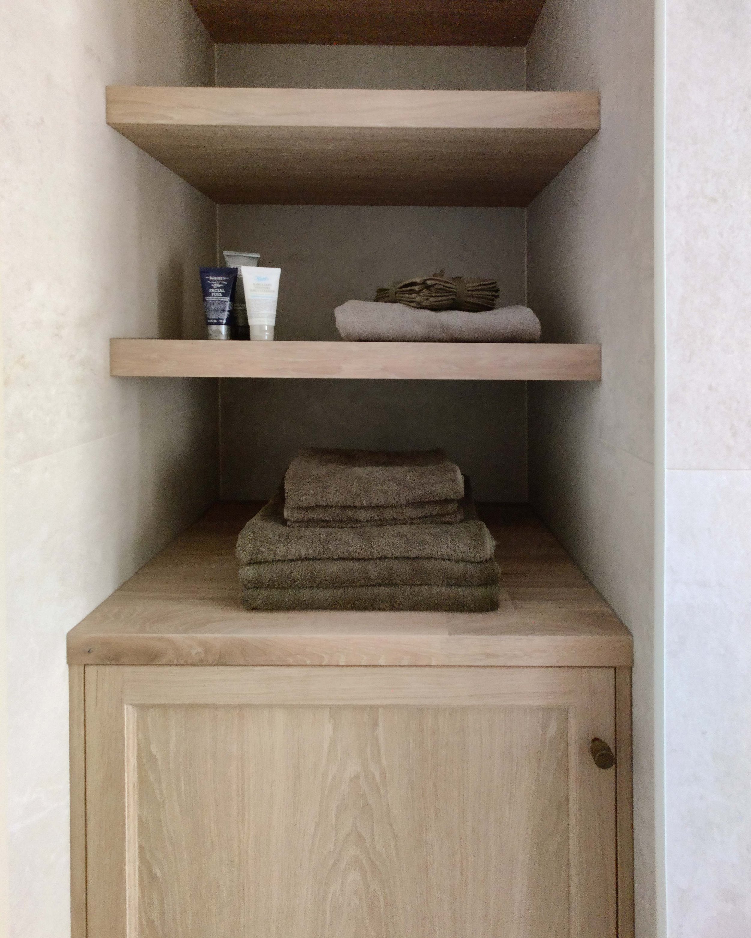 custom made oak bathroom joinery with shelving with simple styling of green towels and toiletries - interior design by Serpentine Interiors