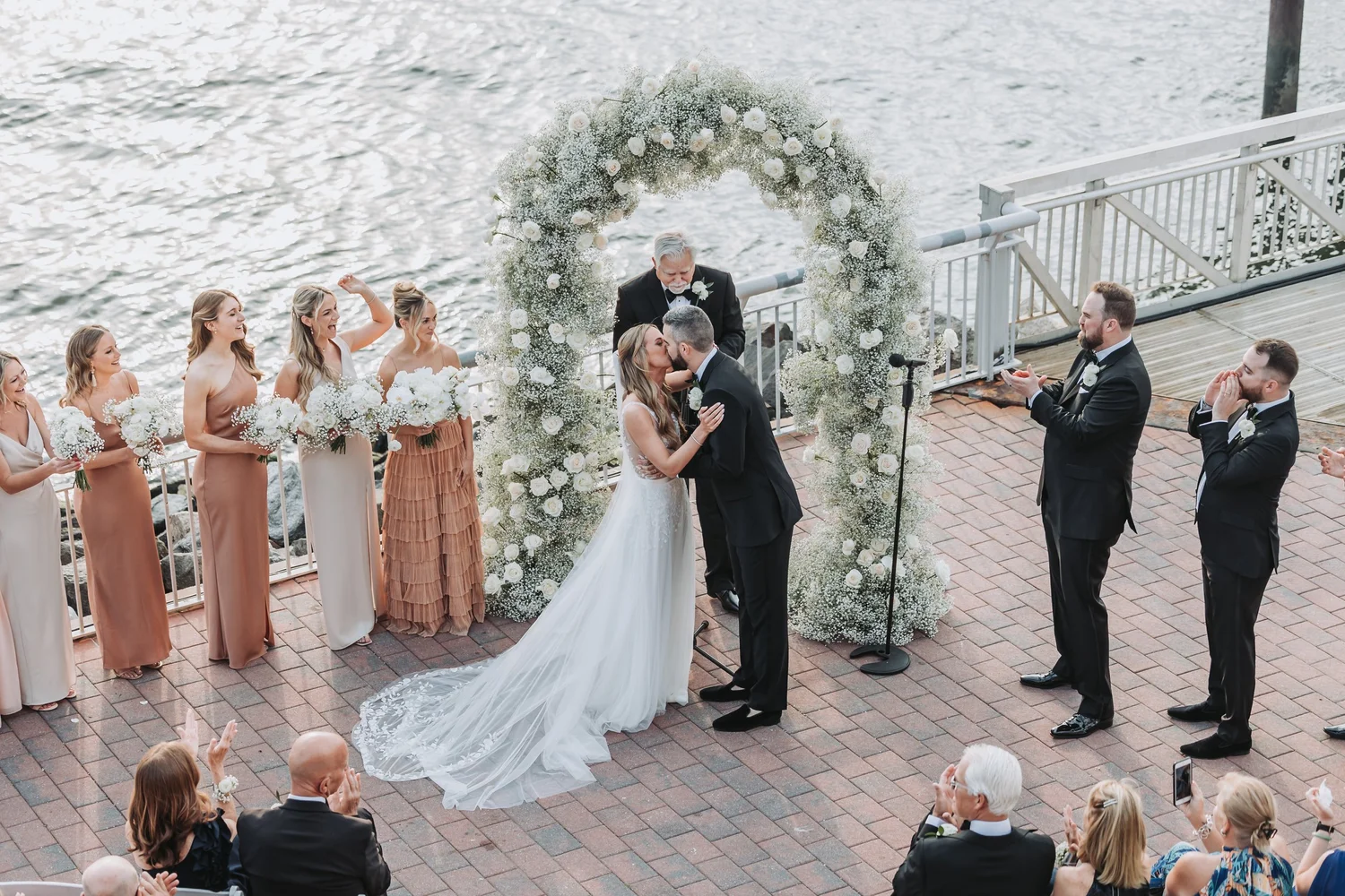 Bride and groom share a moment beneath a floral arch at their waterfront ceremony.