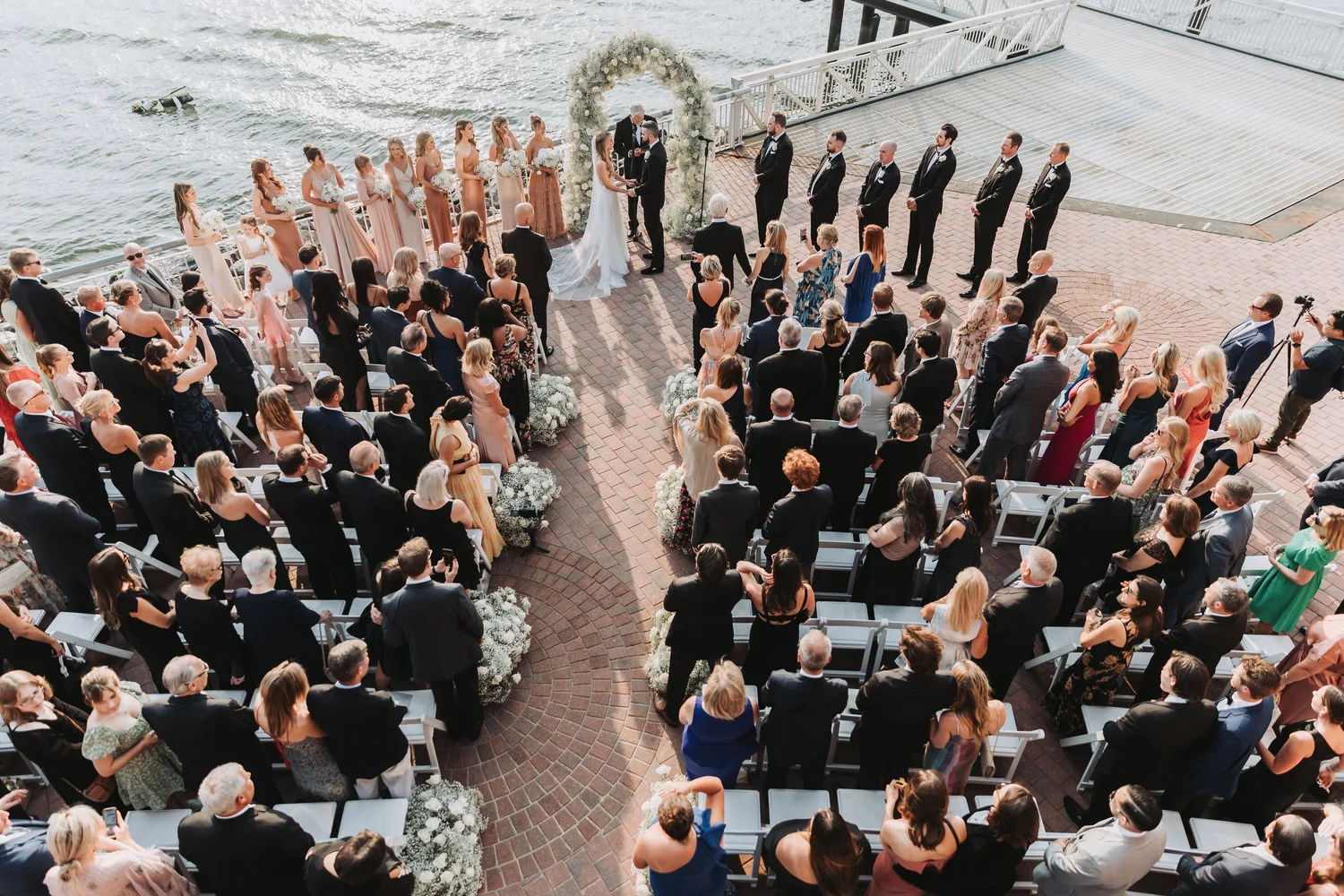 Overhead view of guests seated for an outdoor waterfront wedding ceremony.