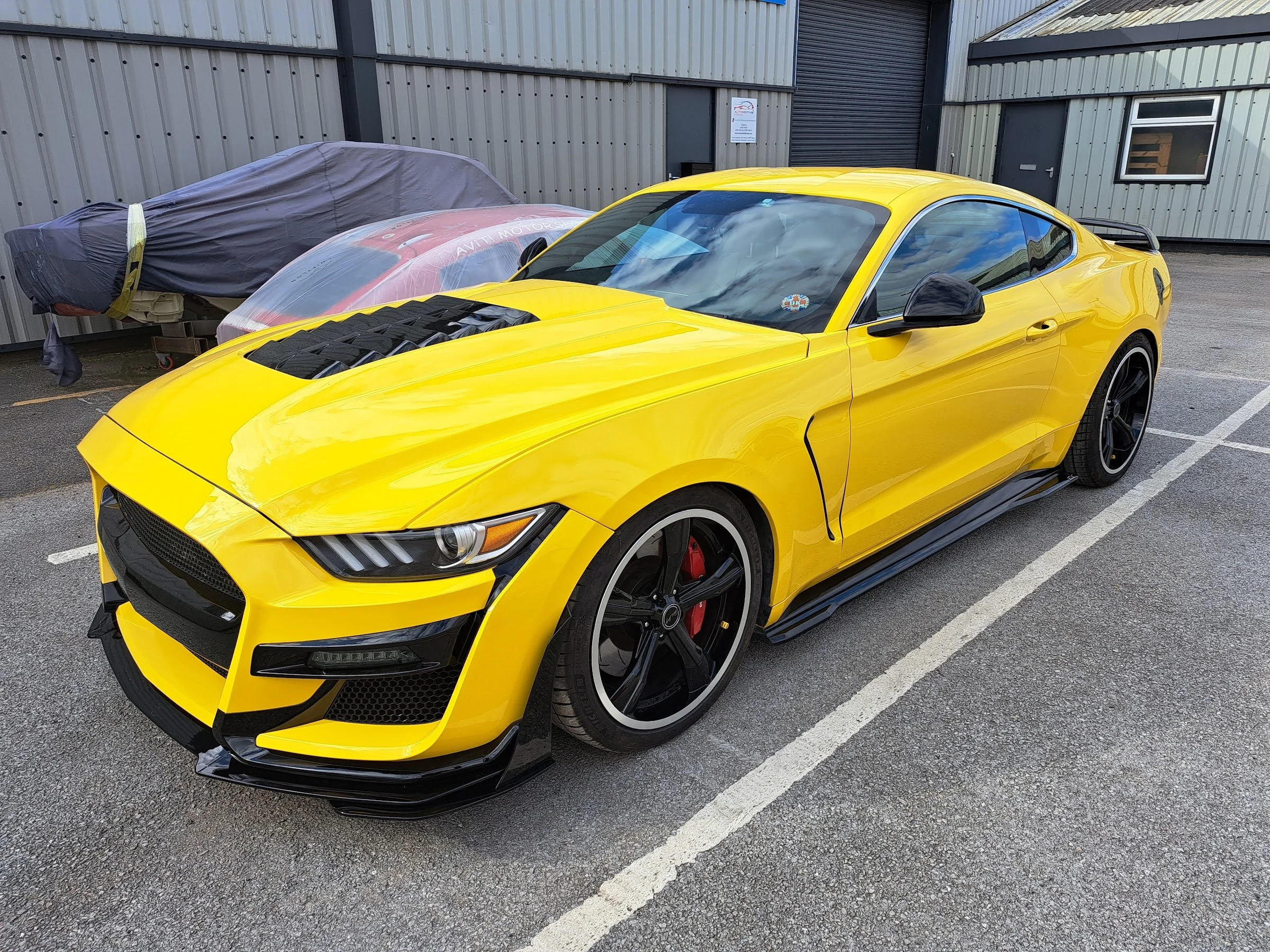 Yellow Ford Mustang with black bonnet vent, front three-quarter view, outside the Automotive Finesse workshop