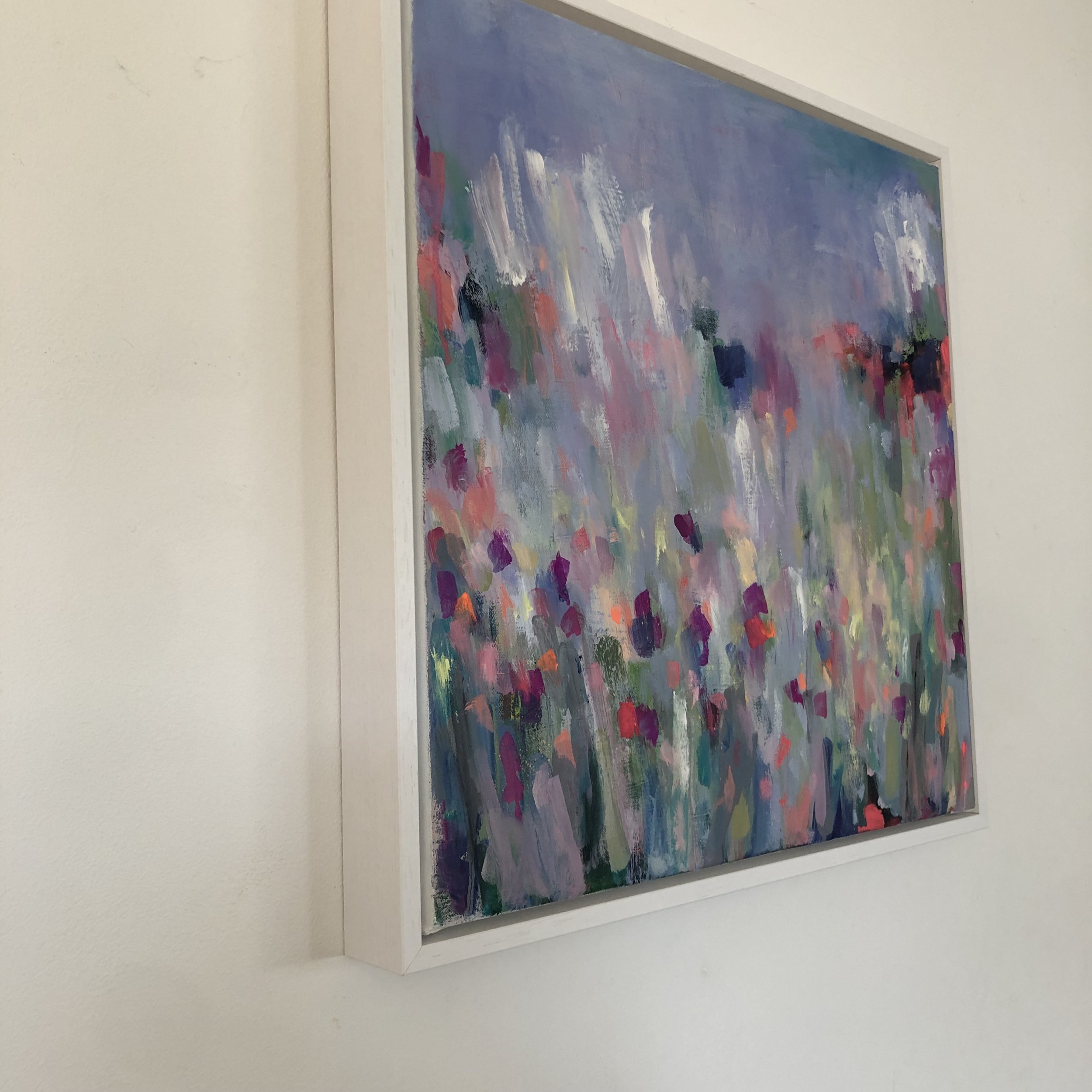 Side view image of painting on a wall in a white tray frame. Vibrant abstract painting showing variety of colours, based on a farm’s driveway covered in wildflowers here in north Wales.