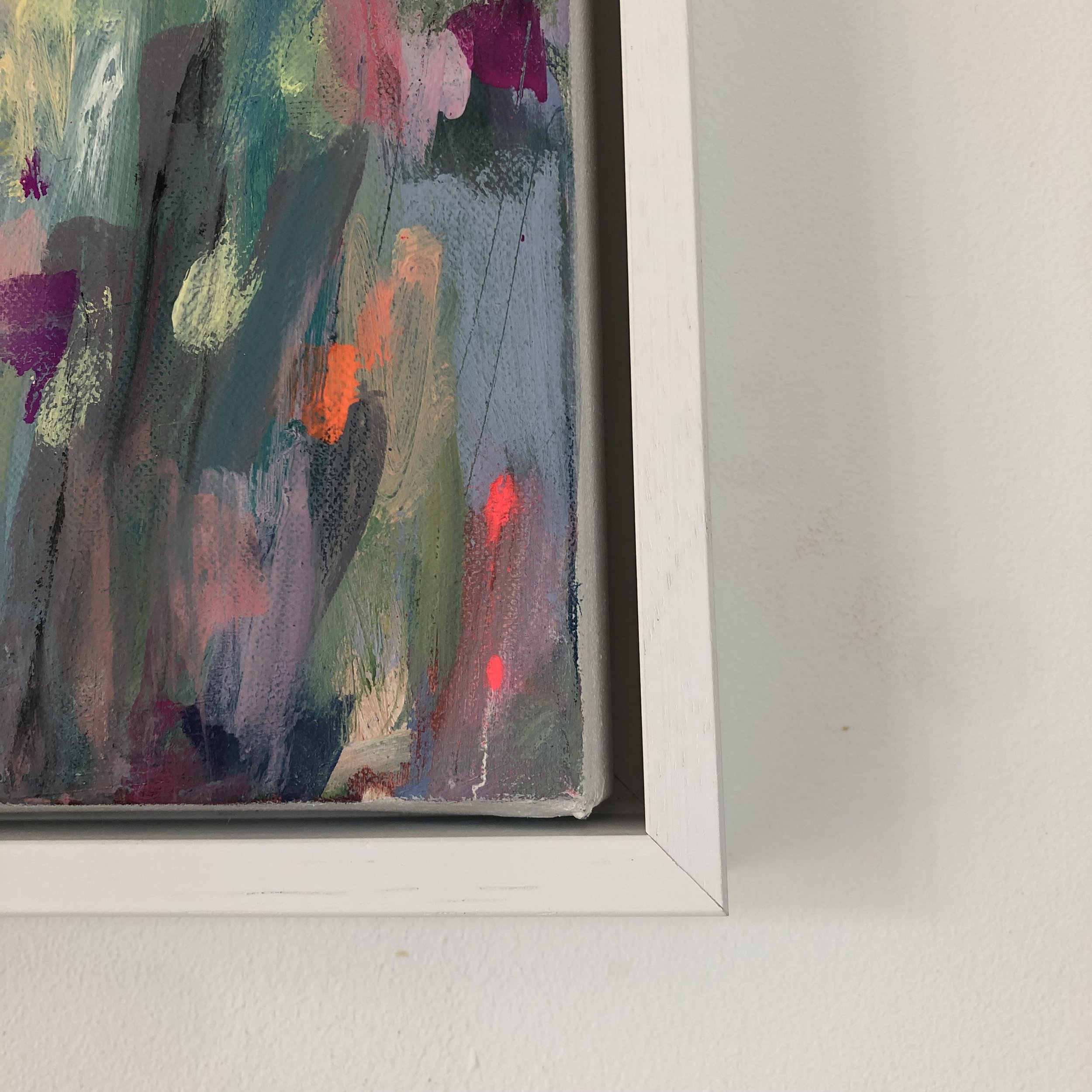 Close up detail of painting on a wall in a white tray frame. Vibrant abstract painting showing variety of colours, based on a farm’s driveway covered in wildflowers here in north Wales.