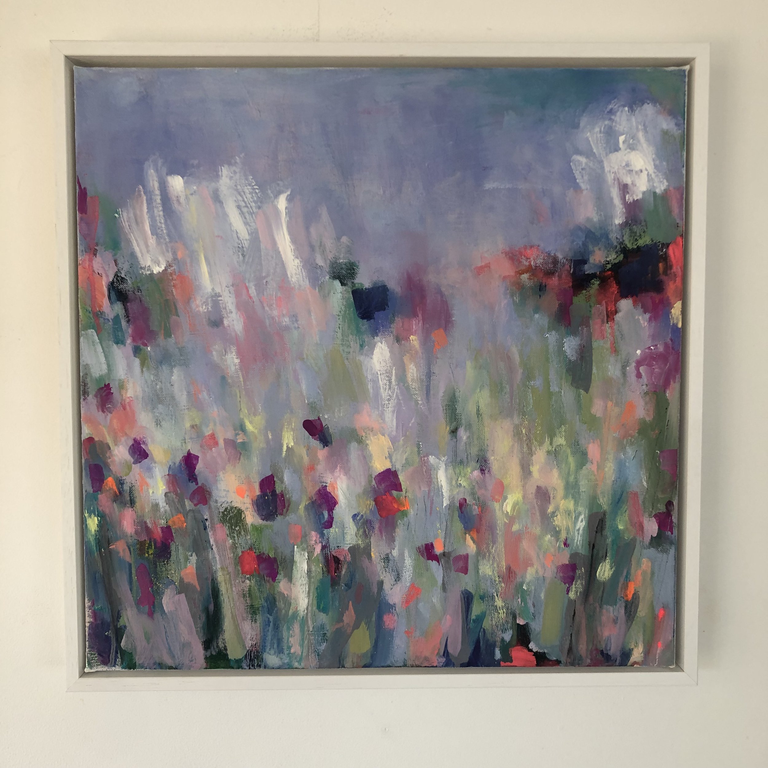 Image of painting on a wall in a white tray frame. Vibrant abstract painting showing variety of colours, based on a farm’s driveway covered in wildflowers here in north Wales.