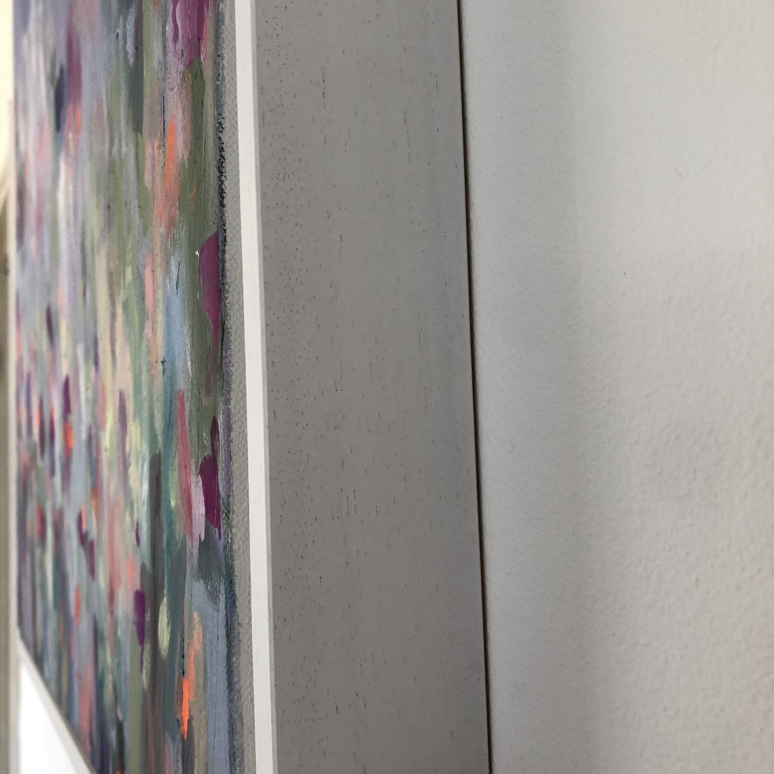 Close-up detail of painting on a wall in a white tray frame. Vibrant abstract painting showing variety of colours, based on a farm’s driveway covered in wildflowers here in north Wales.