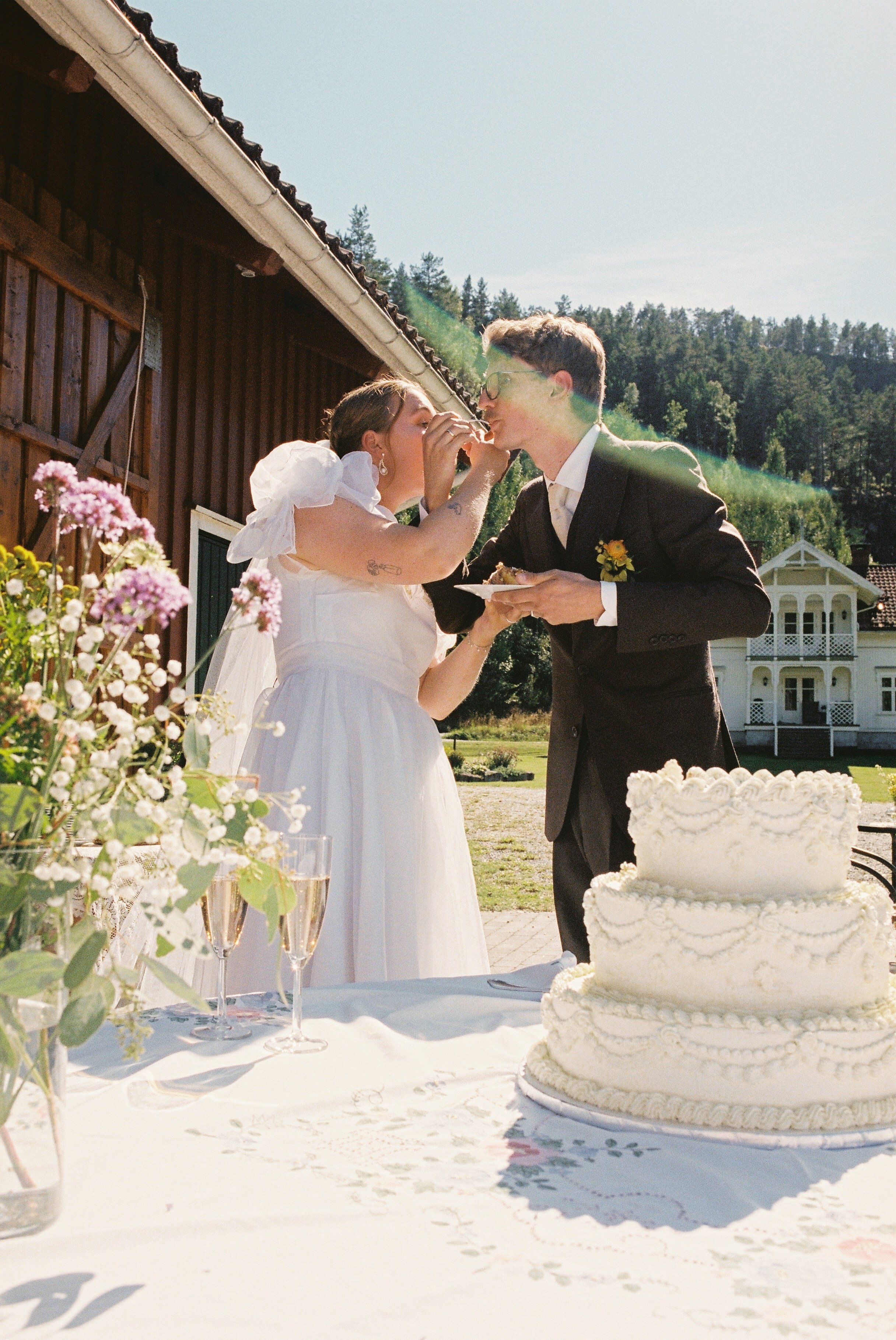 A couple in wedding attire standing on a rocky shoreline by the water, holding hands and looking into the distance.