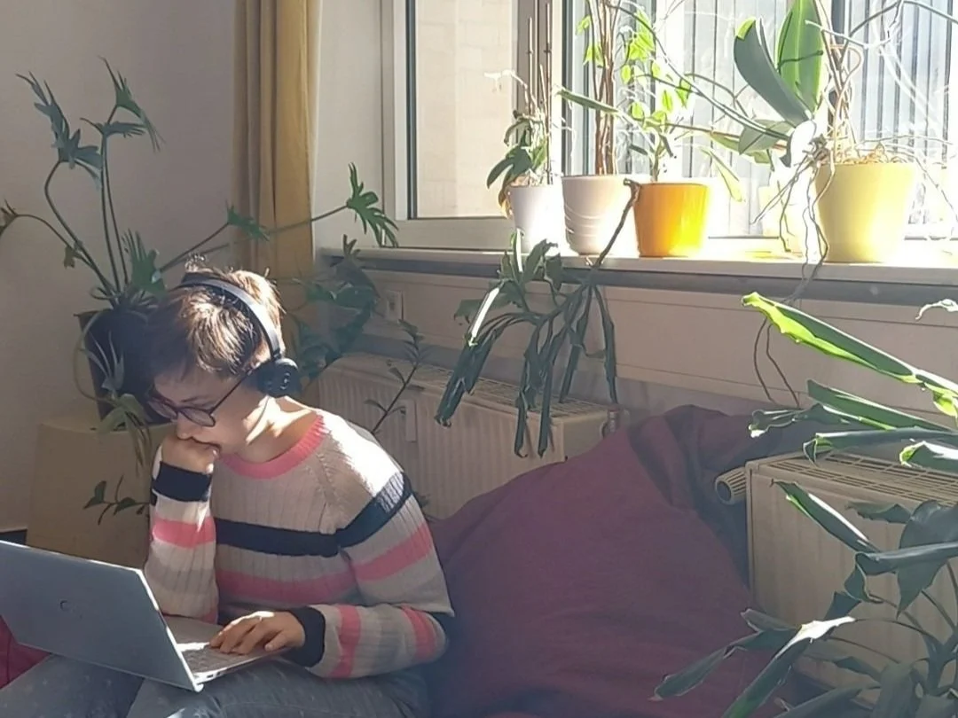 Senka sitzt auf einem Sitzsack am Laptop, in einem lichtdurchfluteten Co-Working-Raum mit vielen Topfpflanzen.