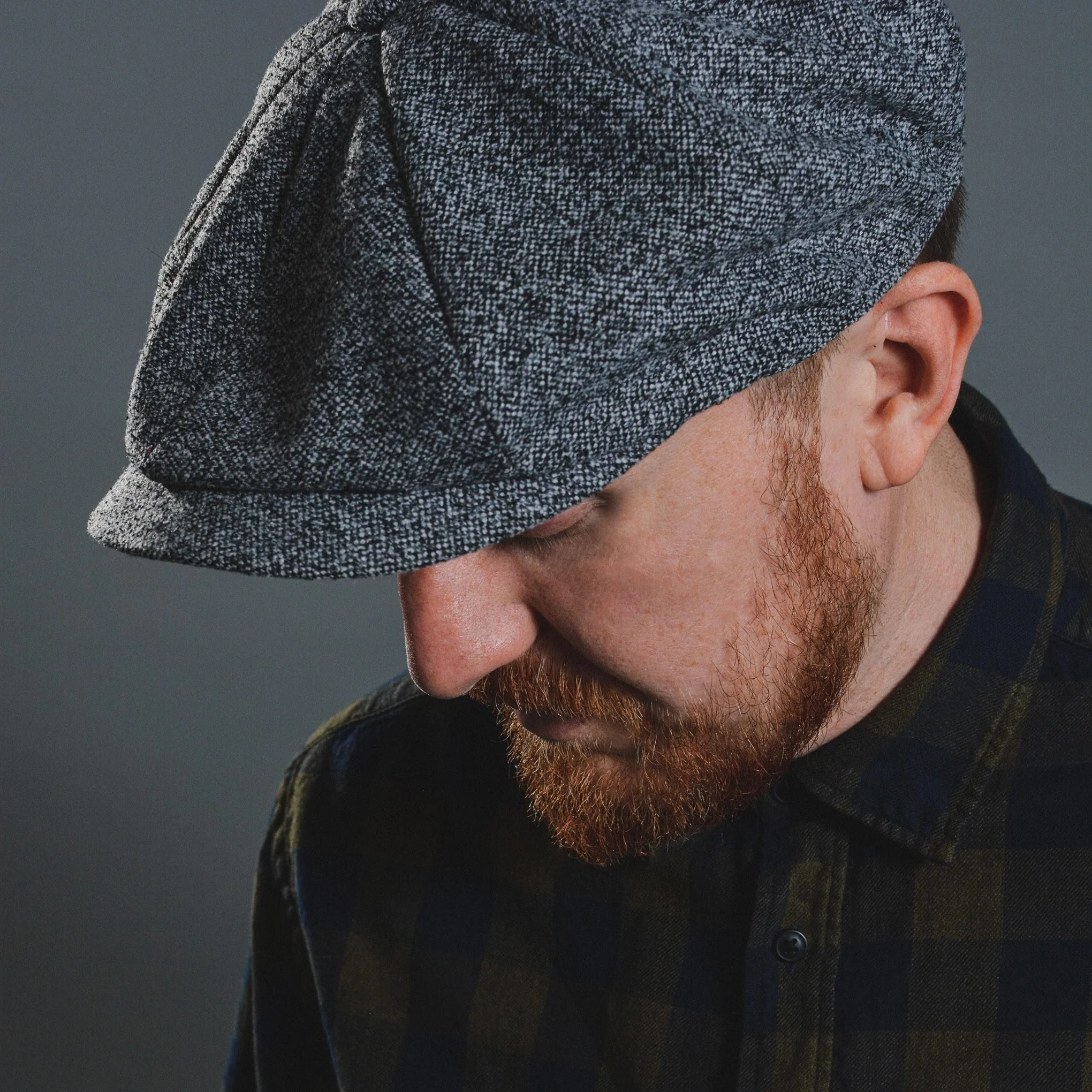 Studio portrait of Griogair wearing a grey flat cap, 2018.