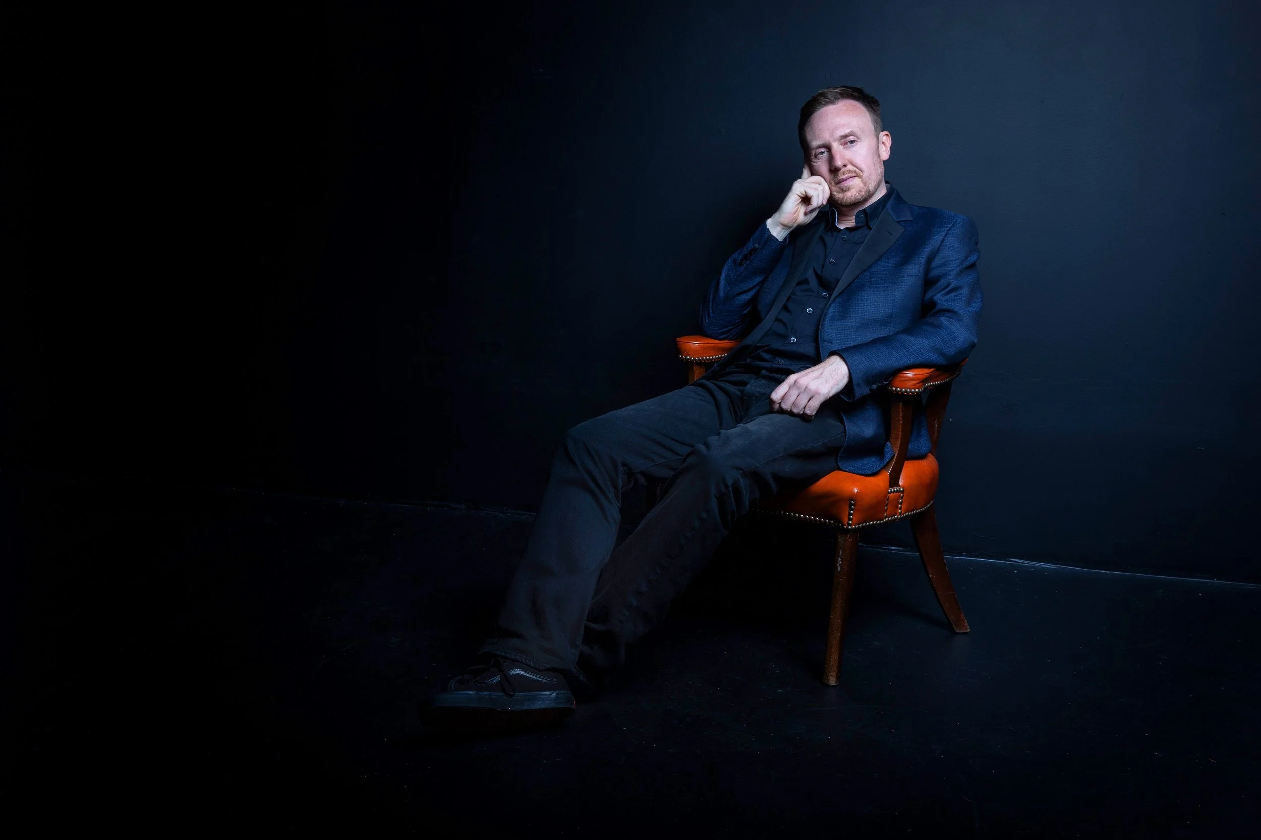 Scottish musician Griogair Labhruidh seated in a dark studio, wearing a dark suit, with a thoughtful expression.