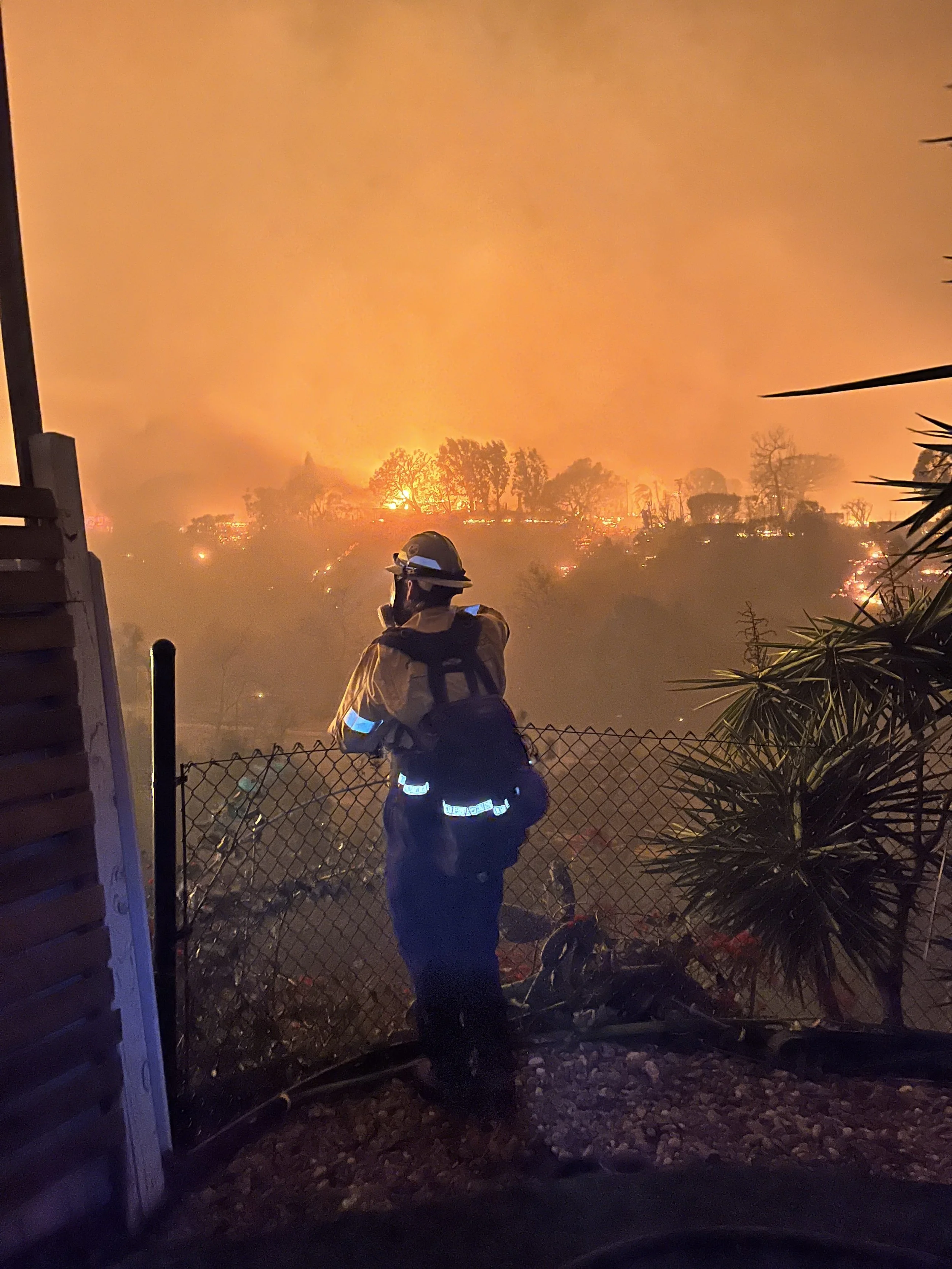 A community brigade member watches the fire burning in Temescal Canyon from Tyler Hauptman’s backyard on Jan 7, 2025. 

 Photo Credit: Tyler Hauptman