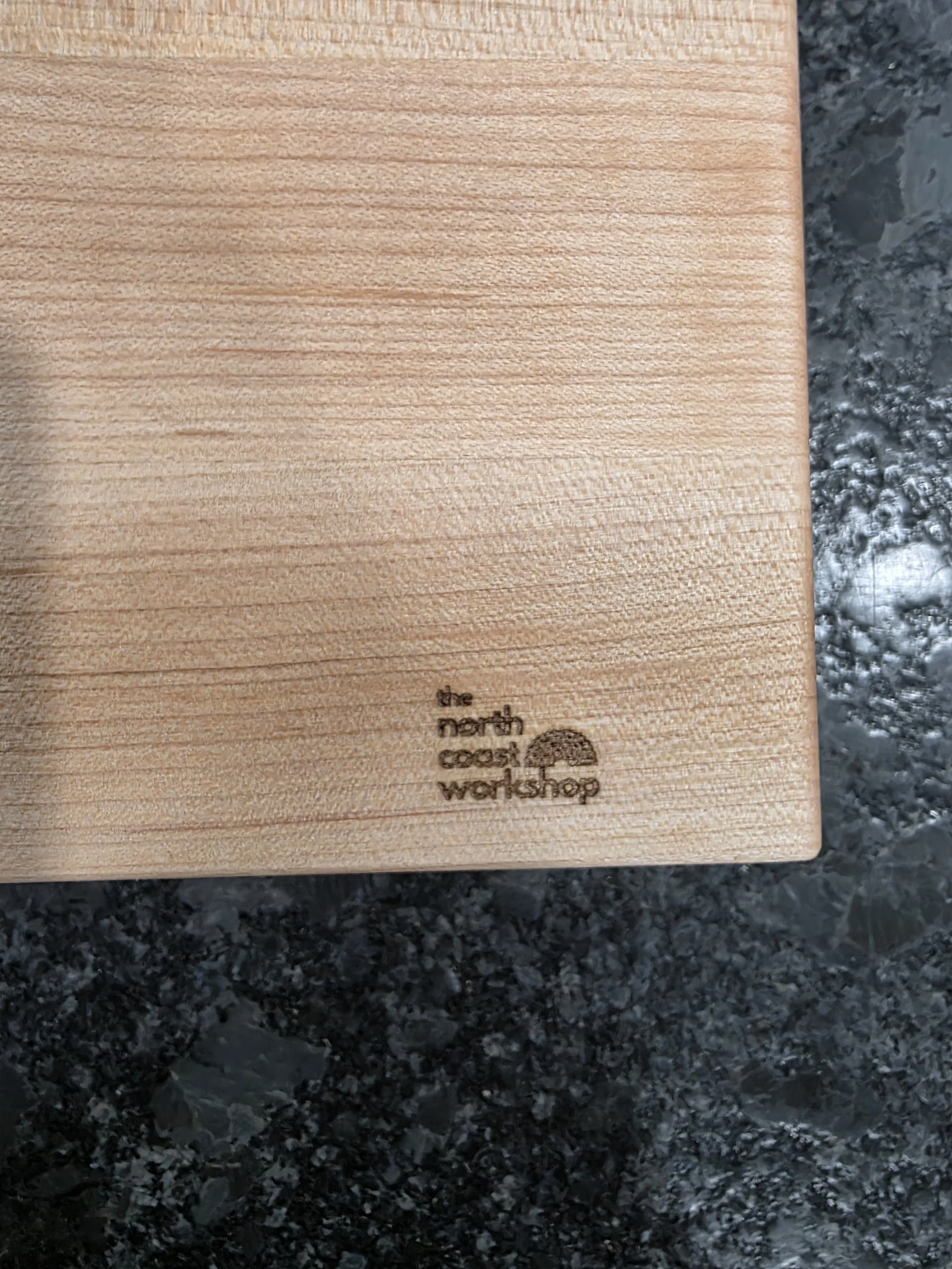 Maple edge grain cutting board close up of The North Coast Workshop logo.