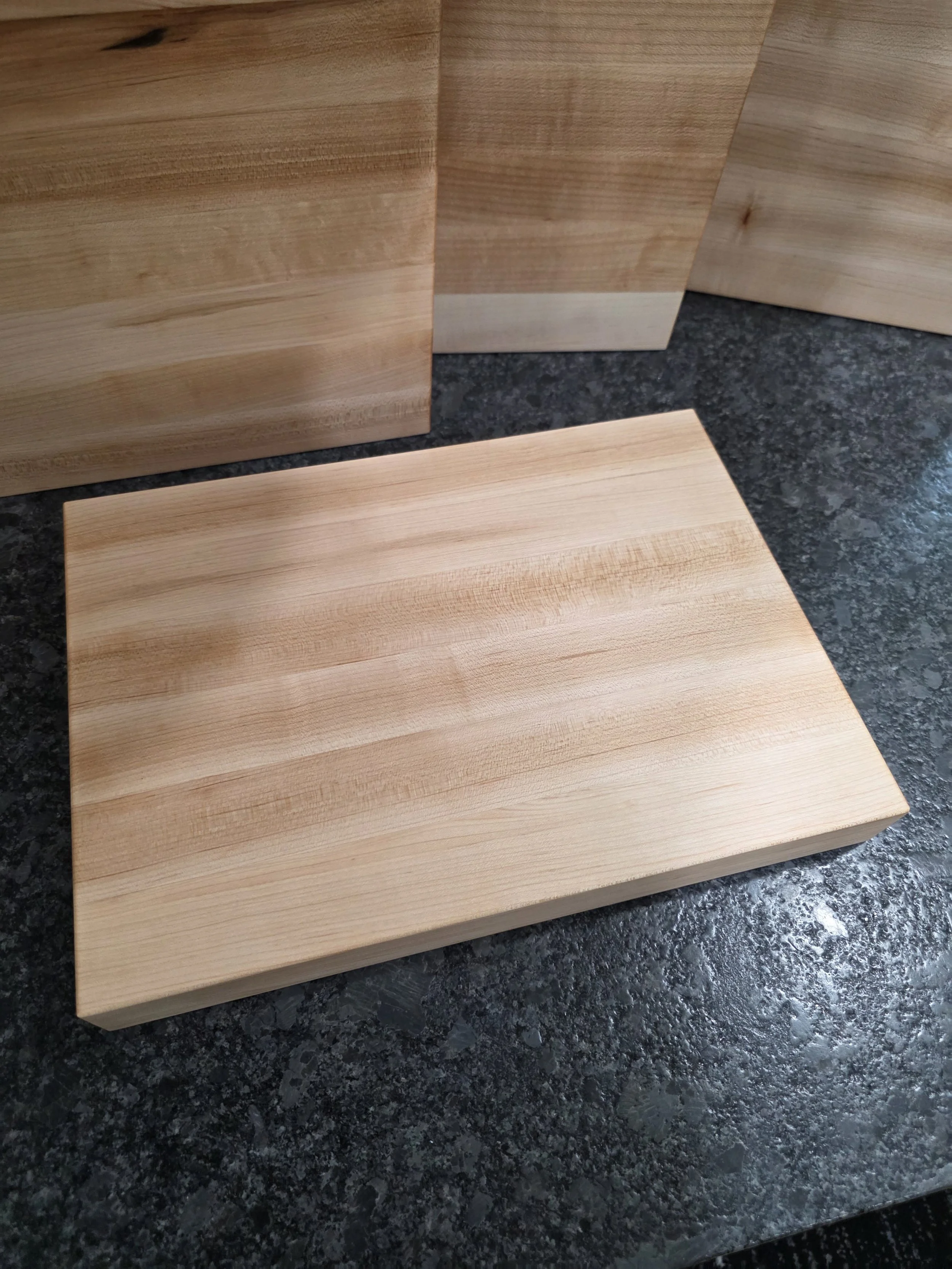 Solid maple edge grain cutting board on counter with boards in background.