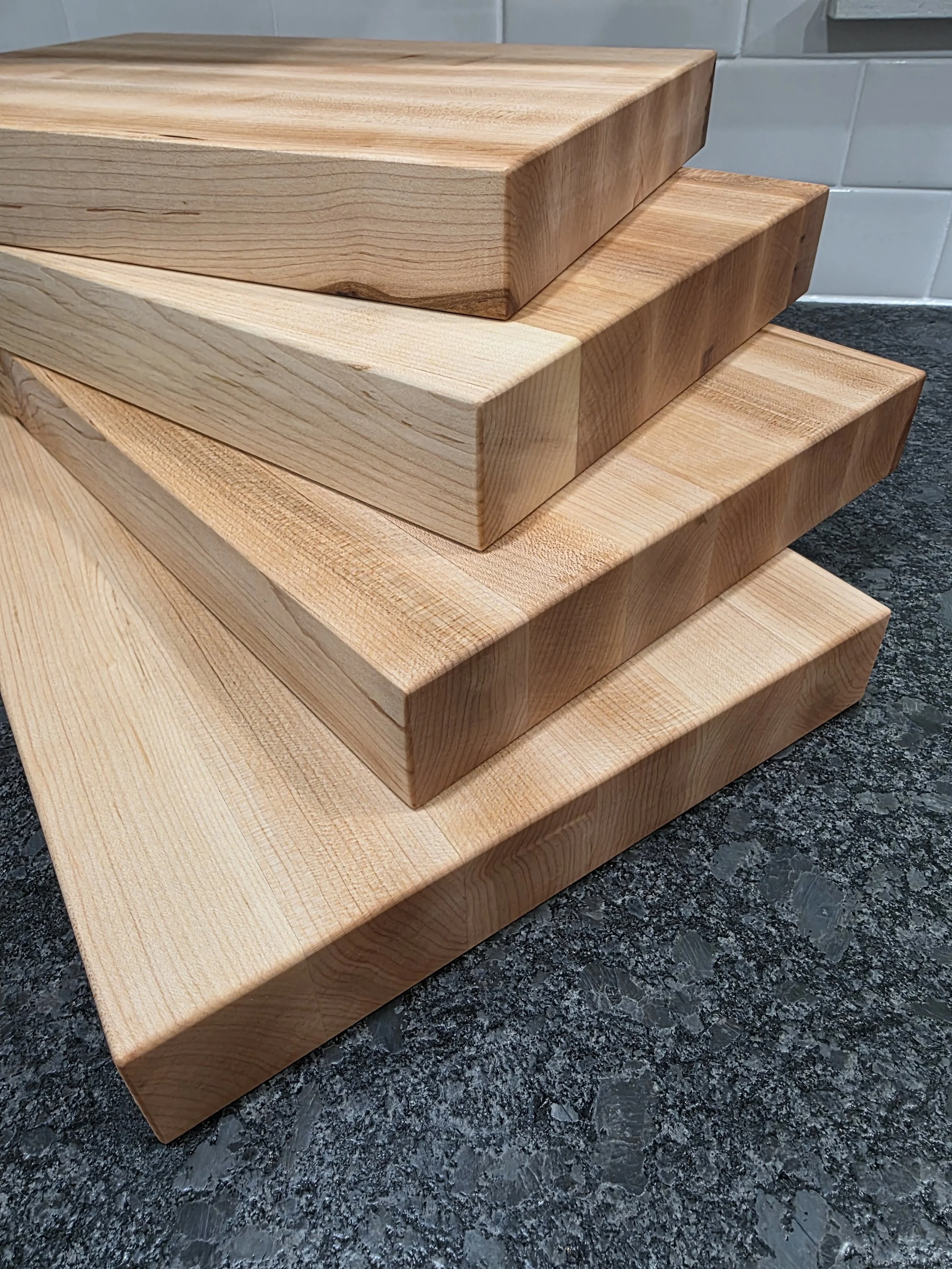 Multiple solid maple edge grain cutting boards stacked on counter.