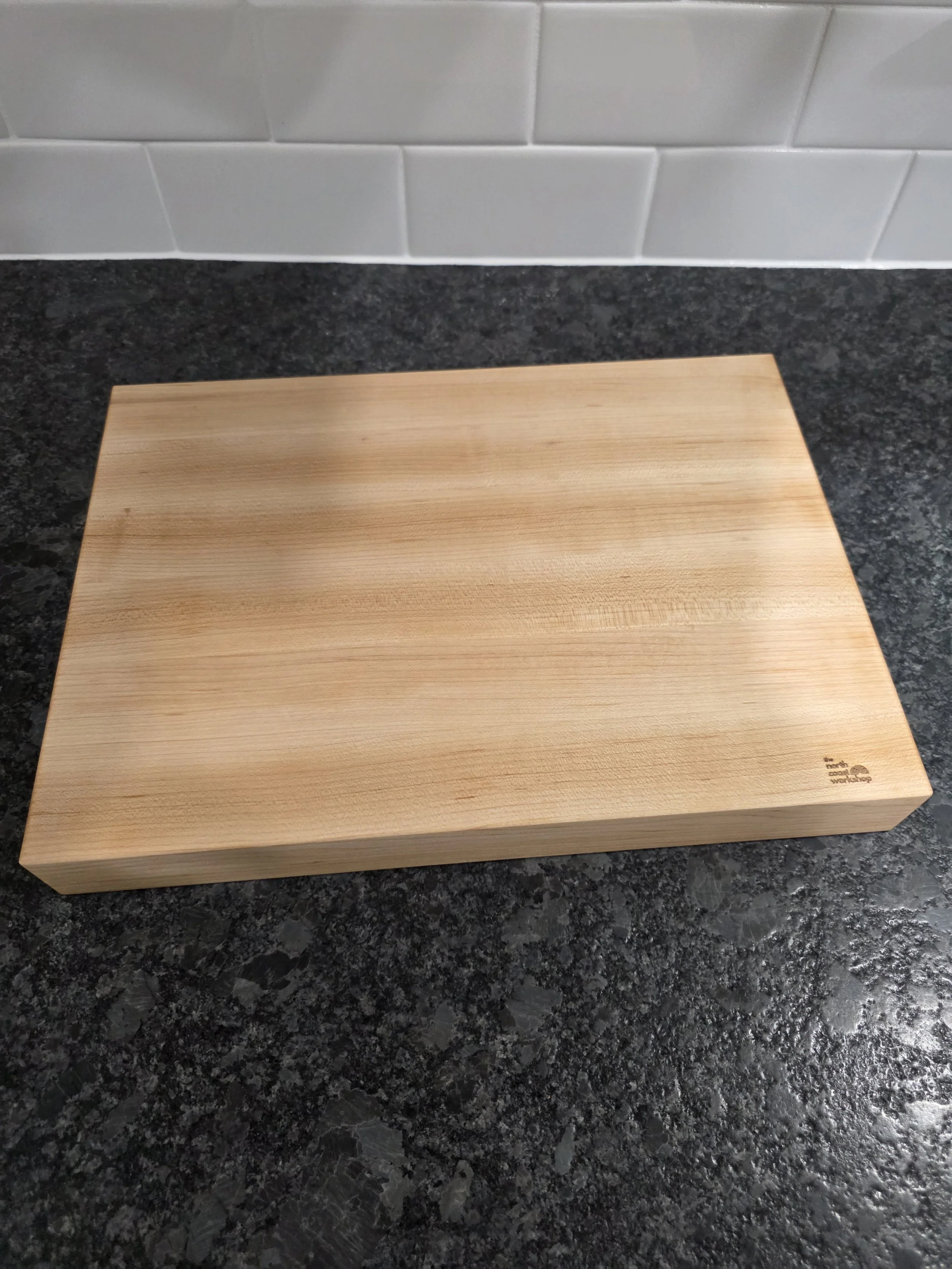 American hard maple edge grain cutting board with The North Coast Workshop logo.