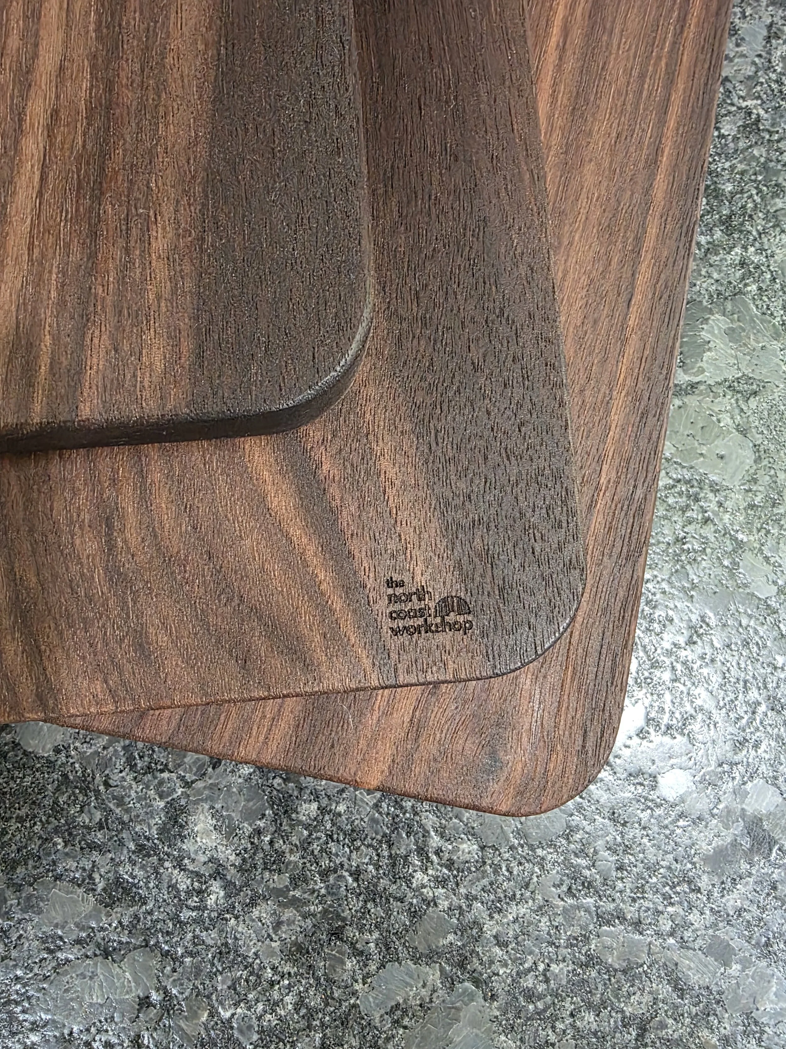 Classic walnut cutting board with close up of The North Coast Workshop Logo.