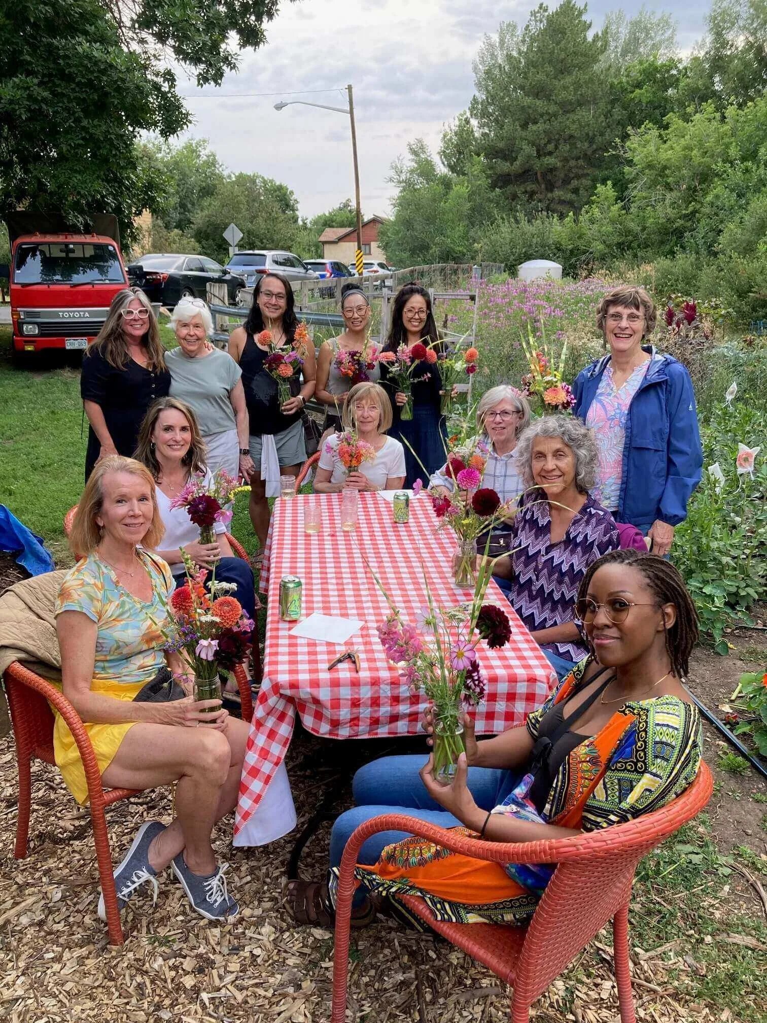 Group of people sitting outdoors at a farm table, each holding a small flower arrangement.