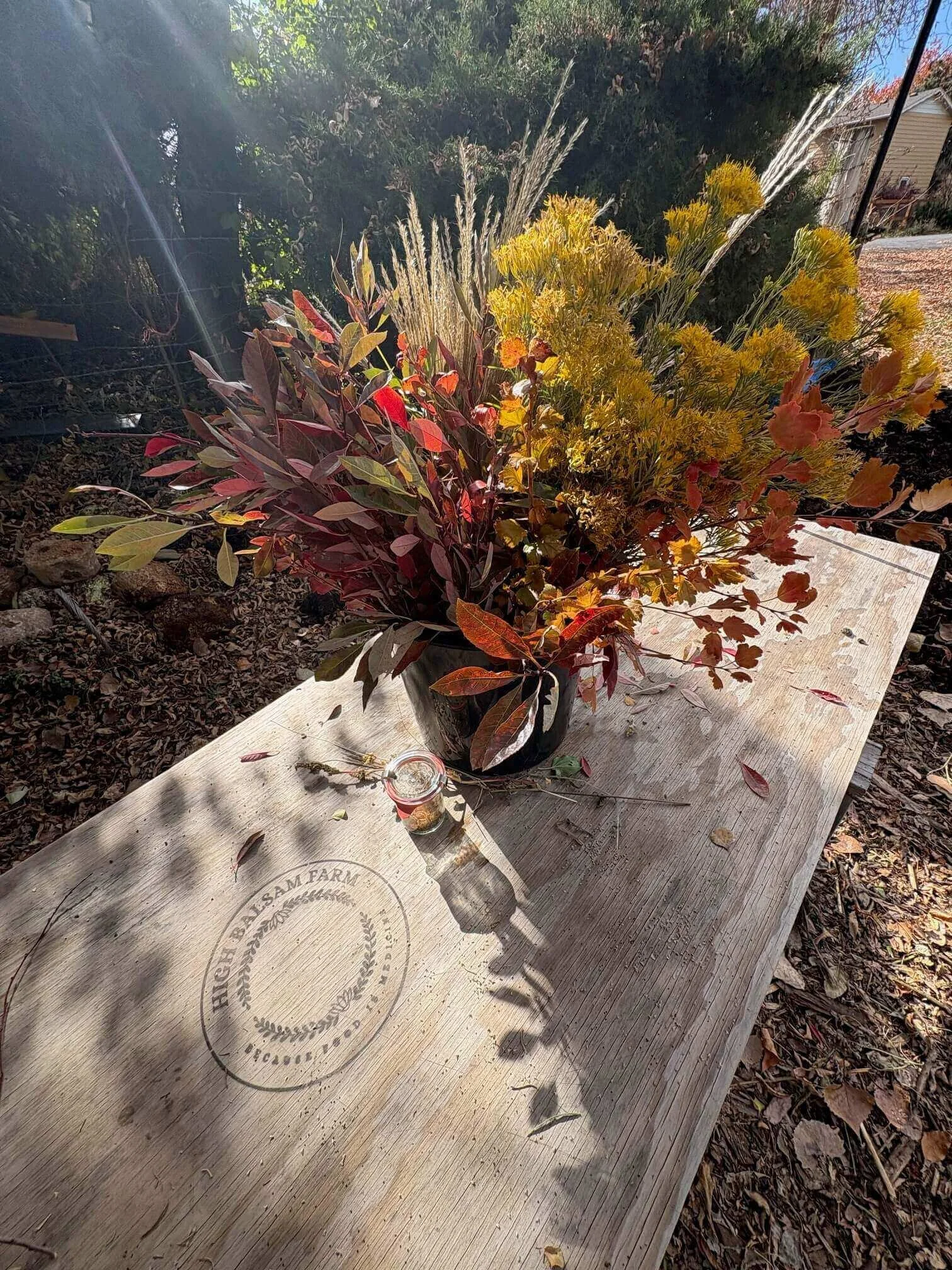 Seasonal foliage and dried flowers arranged in a container on a wooden farm table