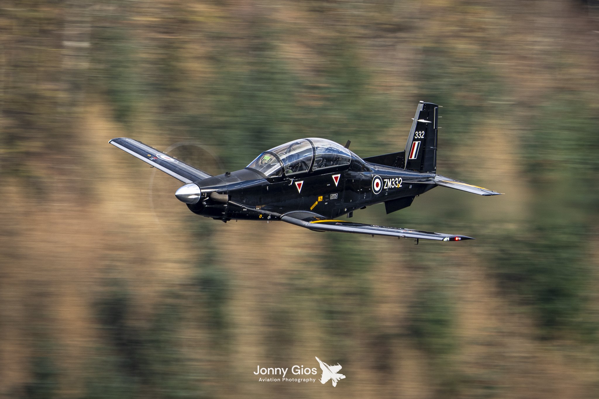 A black jet aircraft flying at high speed over a blurred landscape background.