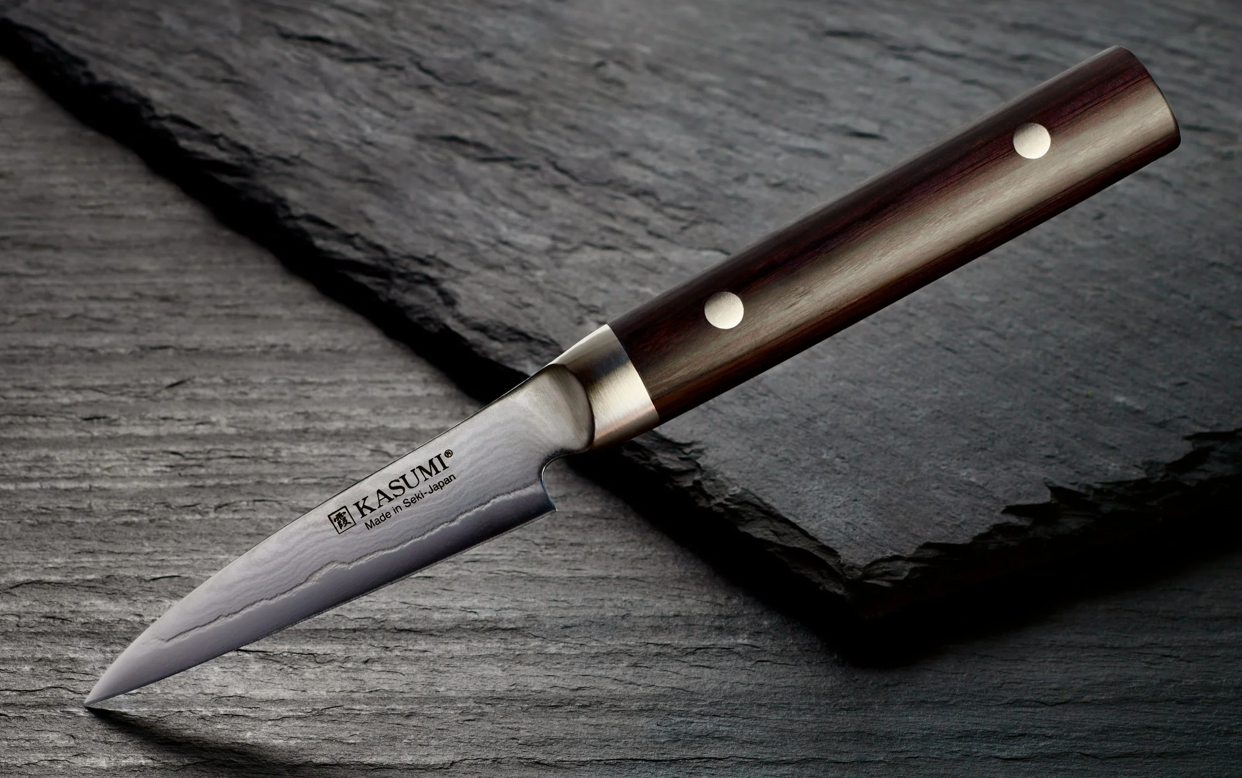 Kasumi Paring Knife floats in the air with the point resting on a bed of slate. The blade design is highlighted with careful lighting by Amy Roth, product photographer in NJ.