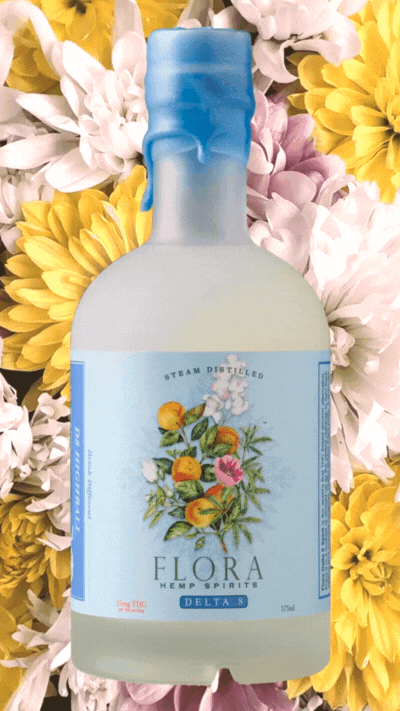 A bed of flowers rotates in the background of a stationary bottle of Flora Delta 8 hemp spirits. Non-alcoholic drinks photography by Amy Roth.