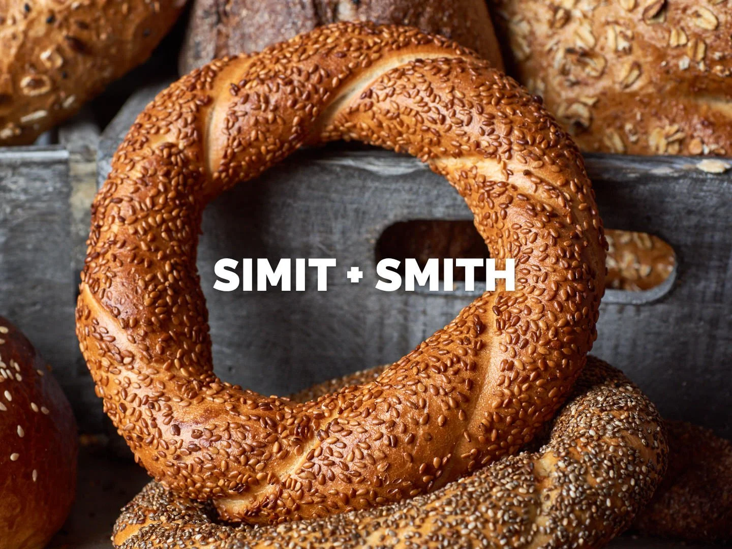 A richly detailed food photography shot showcasing a golden, sesame-crusted simit from Simit + Smith, a brand specializing in traditional Turkish baked goods. This image highlights the artisanal texture, crisp crust, and deep, warm tones of the bread