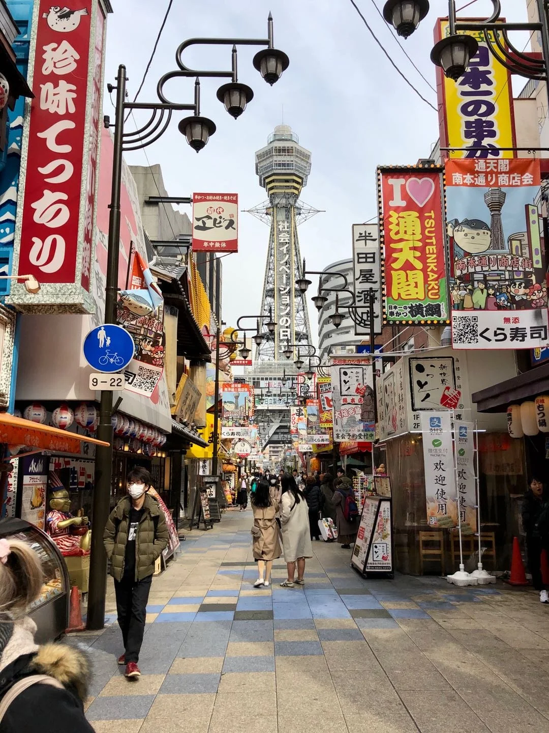 Tsutenkaku tower overlooking a busy street in the Shinsekai neighborhood of Osaka, Japan.