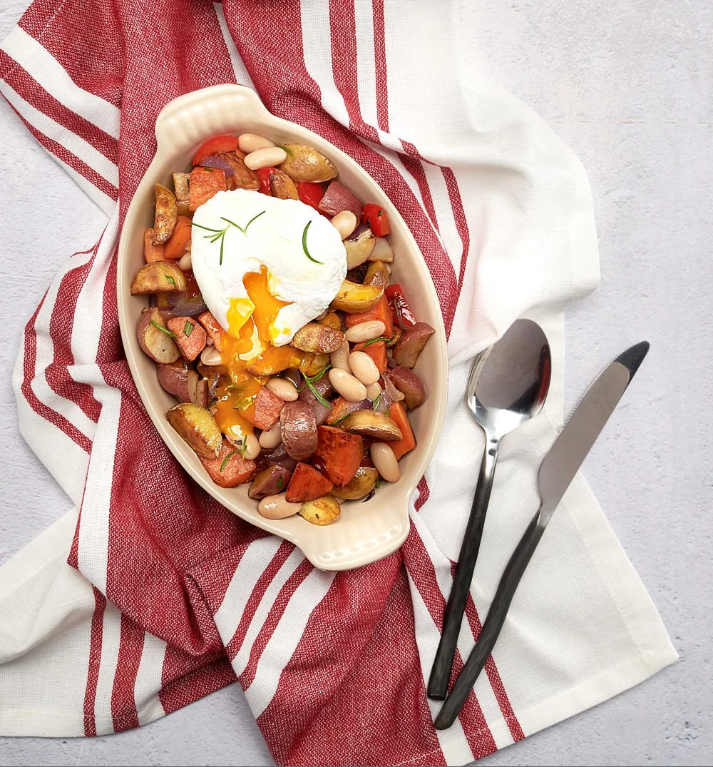 Overhead photo of Born Free poached egg with runny yolk over corned beef hash, served in a small dish sitting on a red and white napkin on a gray stone surface.