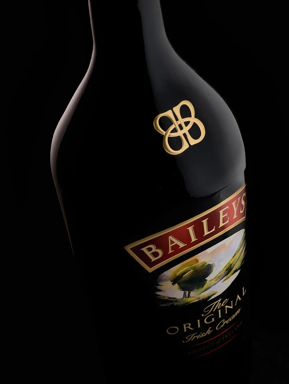 A bottle of Baileys Irish Cream photographed against a black background with soft highlights on the edges of the bottle. It's rotated and presented at an angle, shot down on, so the logo is more prominent than the label.