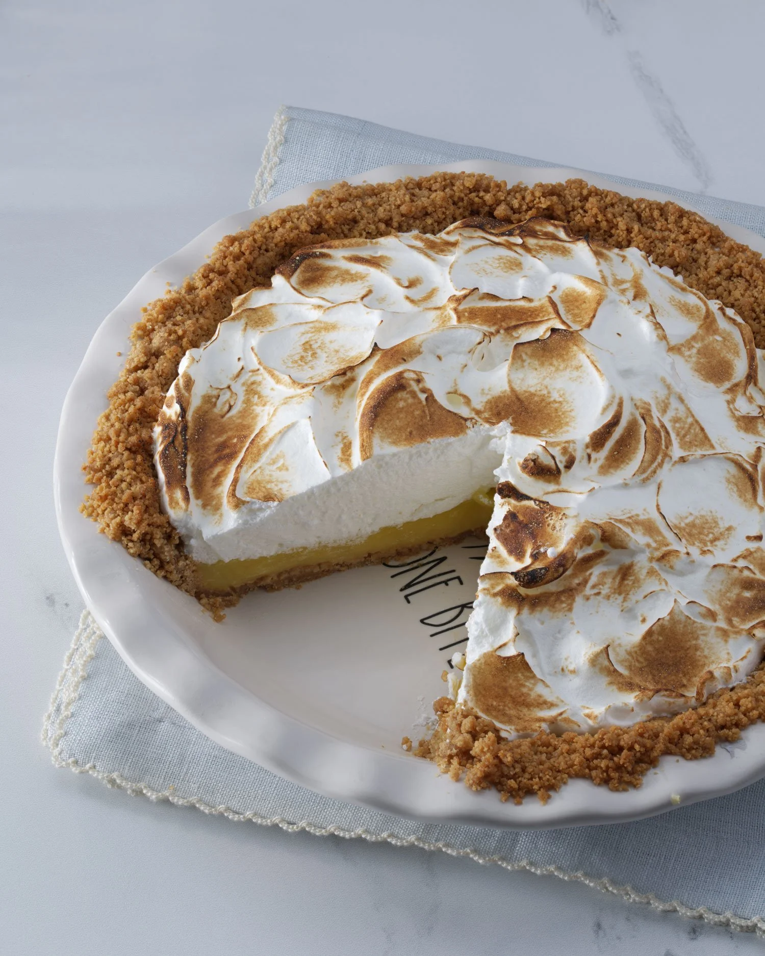 A lemon meringue pie with toasted meringue topping on a white plate with the words