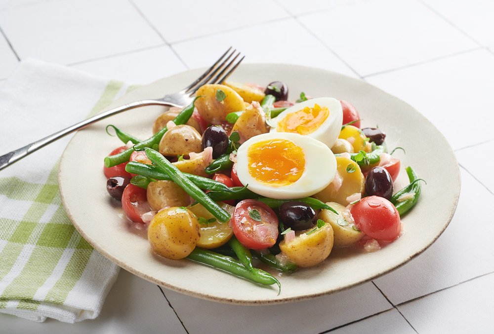 Dressed salad in a shallow white bowl topped with Born Free jammy soft-boiled eggs, halved.