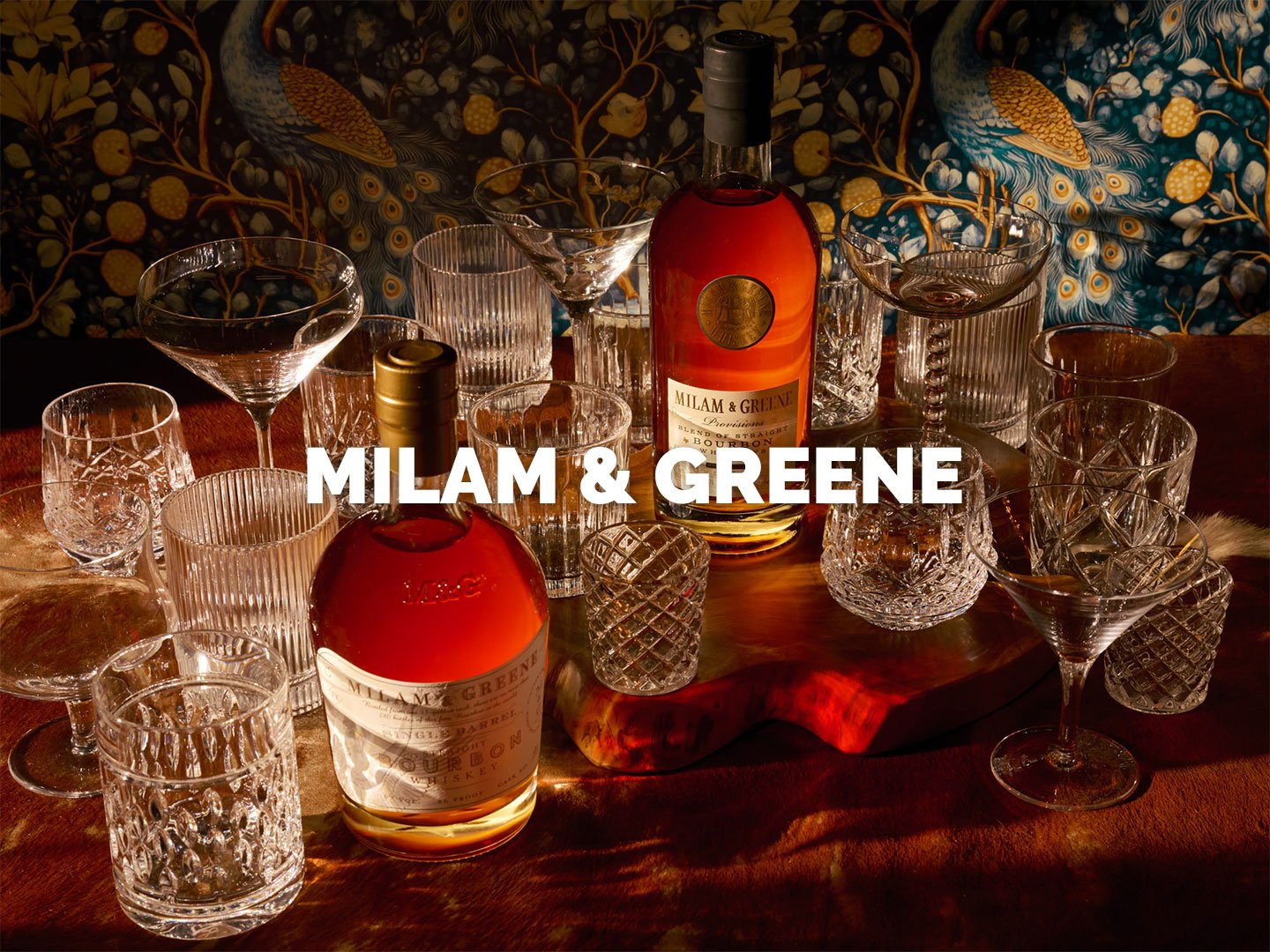 Commercial whiskey photography of Milam & Greene featuring bourbon and rye bottles styled among curated glassware and warm, textured surfaces, using intentional lighting and refined art direction to convey authenticity, hospitality, and a modern, bra