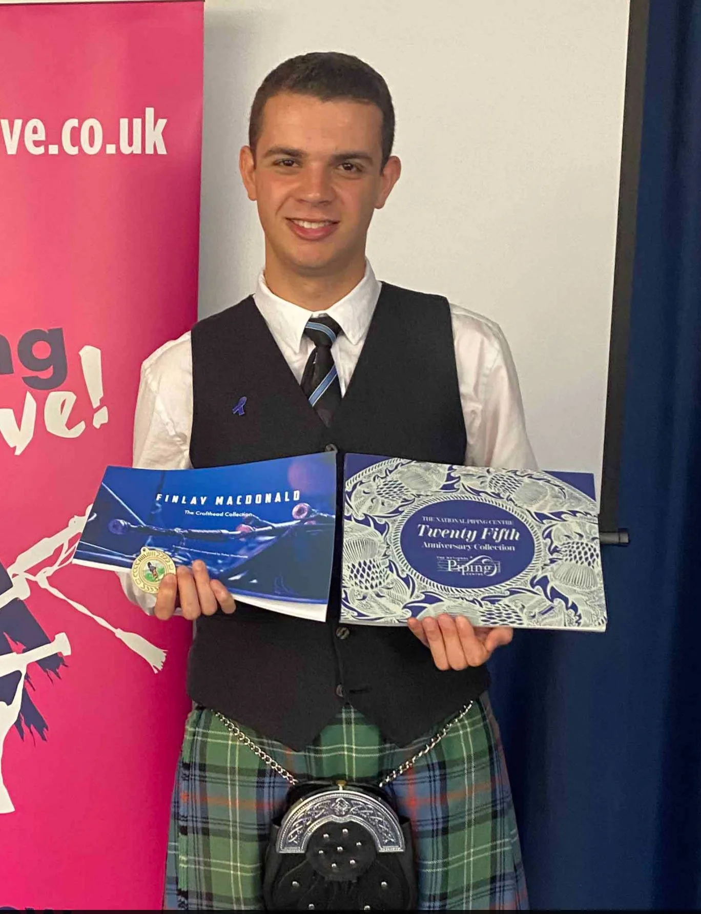 A man wearing glasses with a slight frown, standing in an office environment with books, framed pictures, and a black dog figurine on a table in the background.