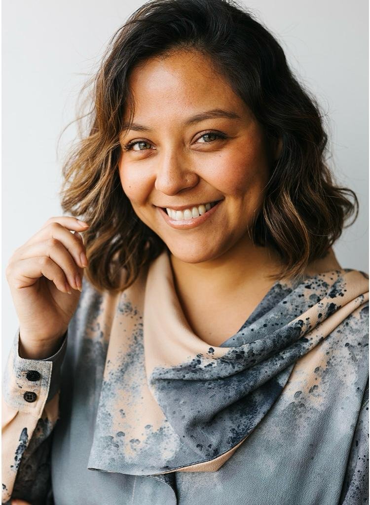 Retrato de una mujer con cabello rizado y rubio, sonriendo y mirando a la cámara, con un fondo claro.