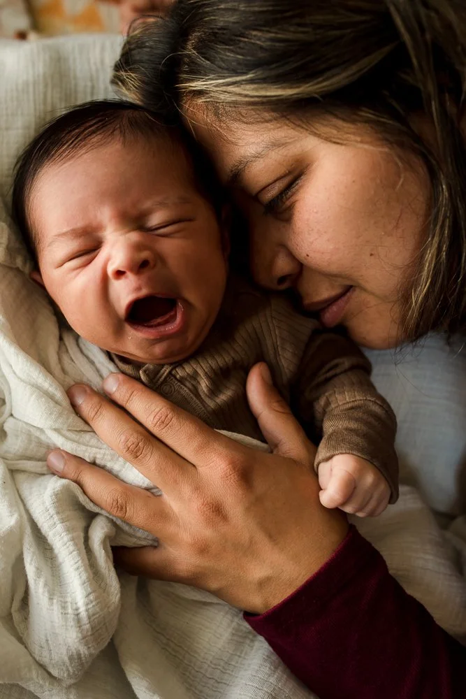 A woman holding a crying baby close to her face, both lying down.