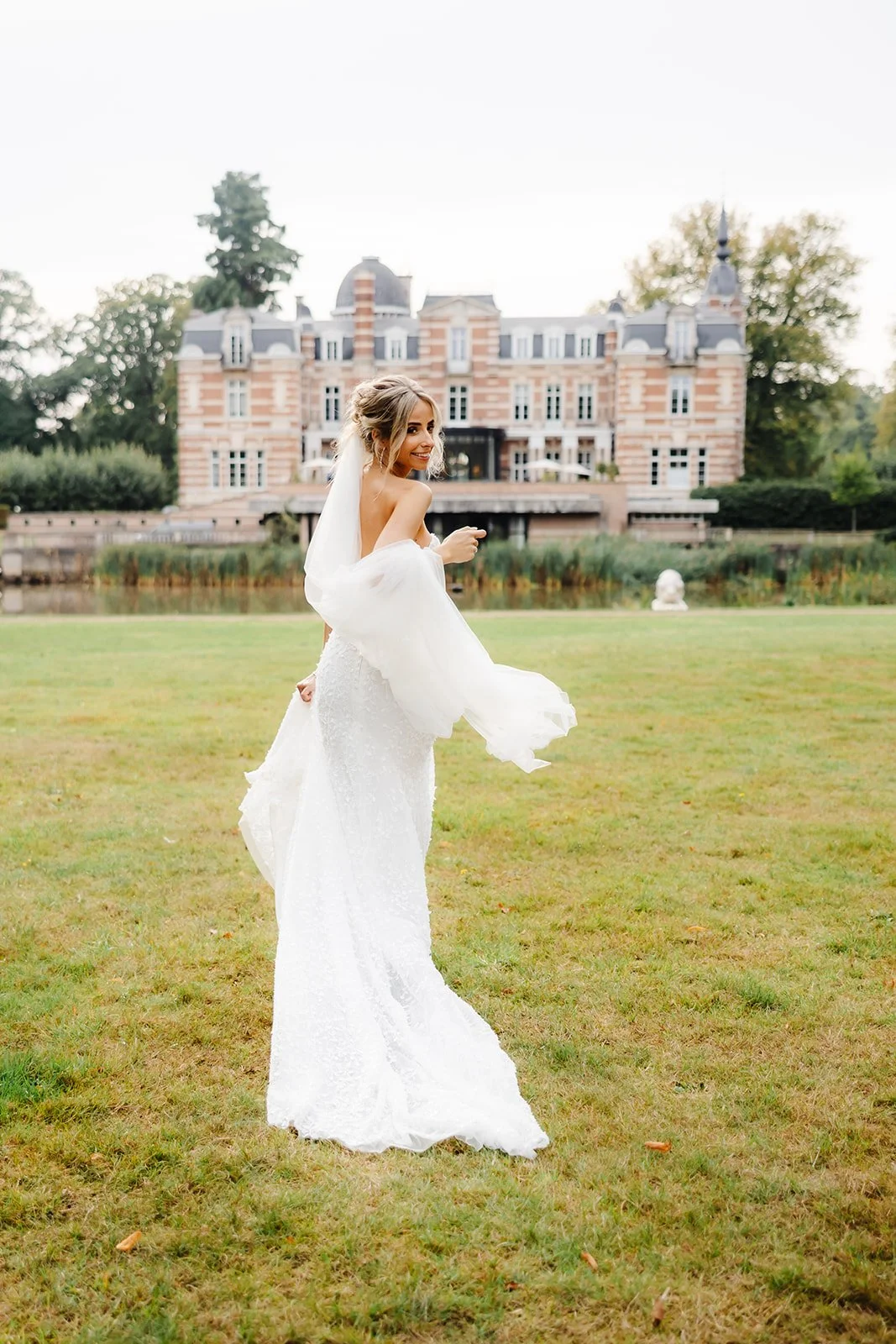 Gelukkig meisje in witte trouwjurk die op een grasveld danst met een kasteel op de achtergrond.