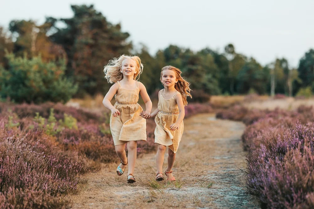 Twee zusjes rennen over het zandpad door de heide