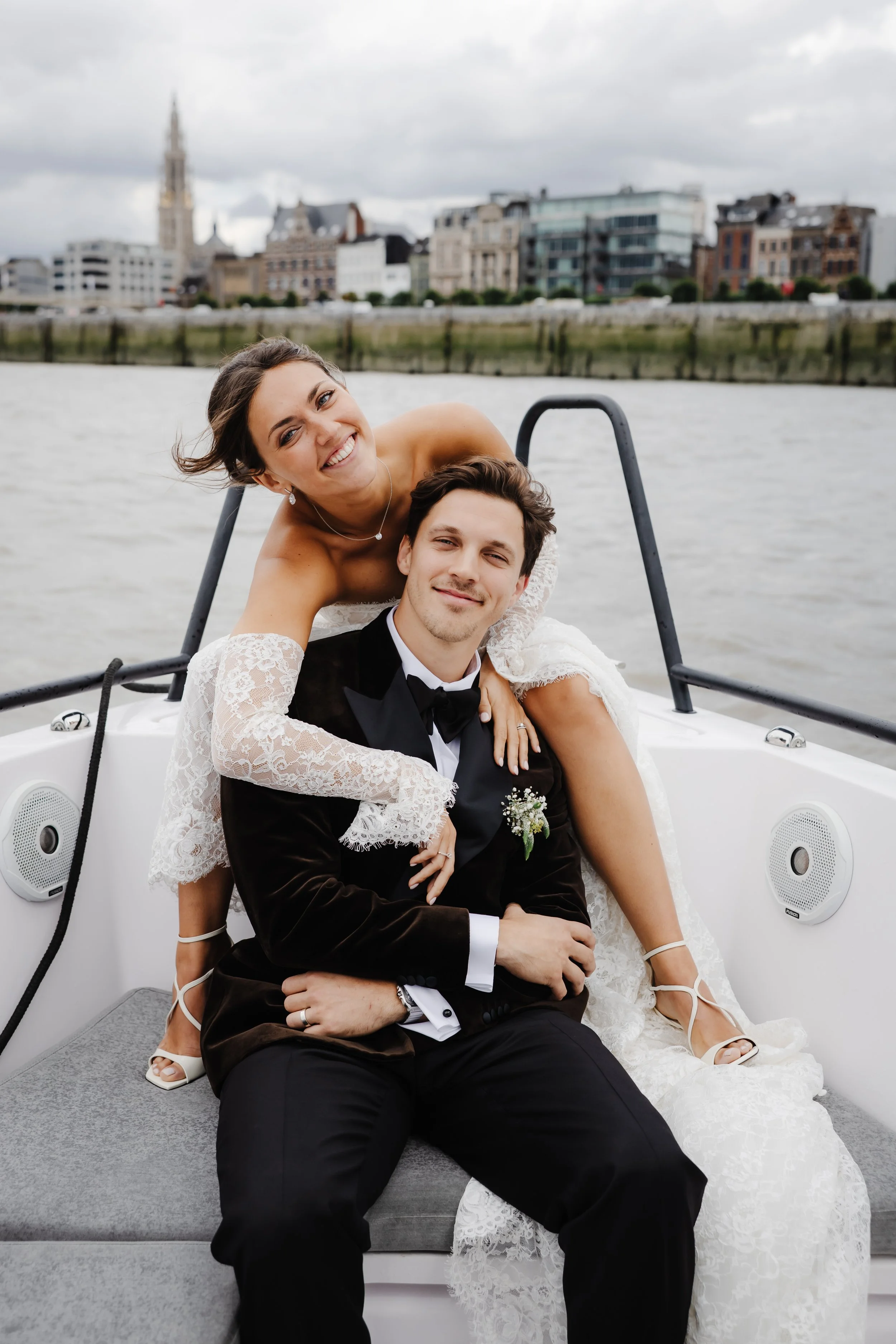 Een bruid en een bruidegom op een boot, met een stad op de achtergrond.