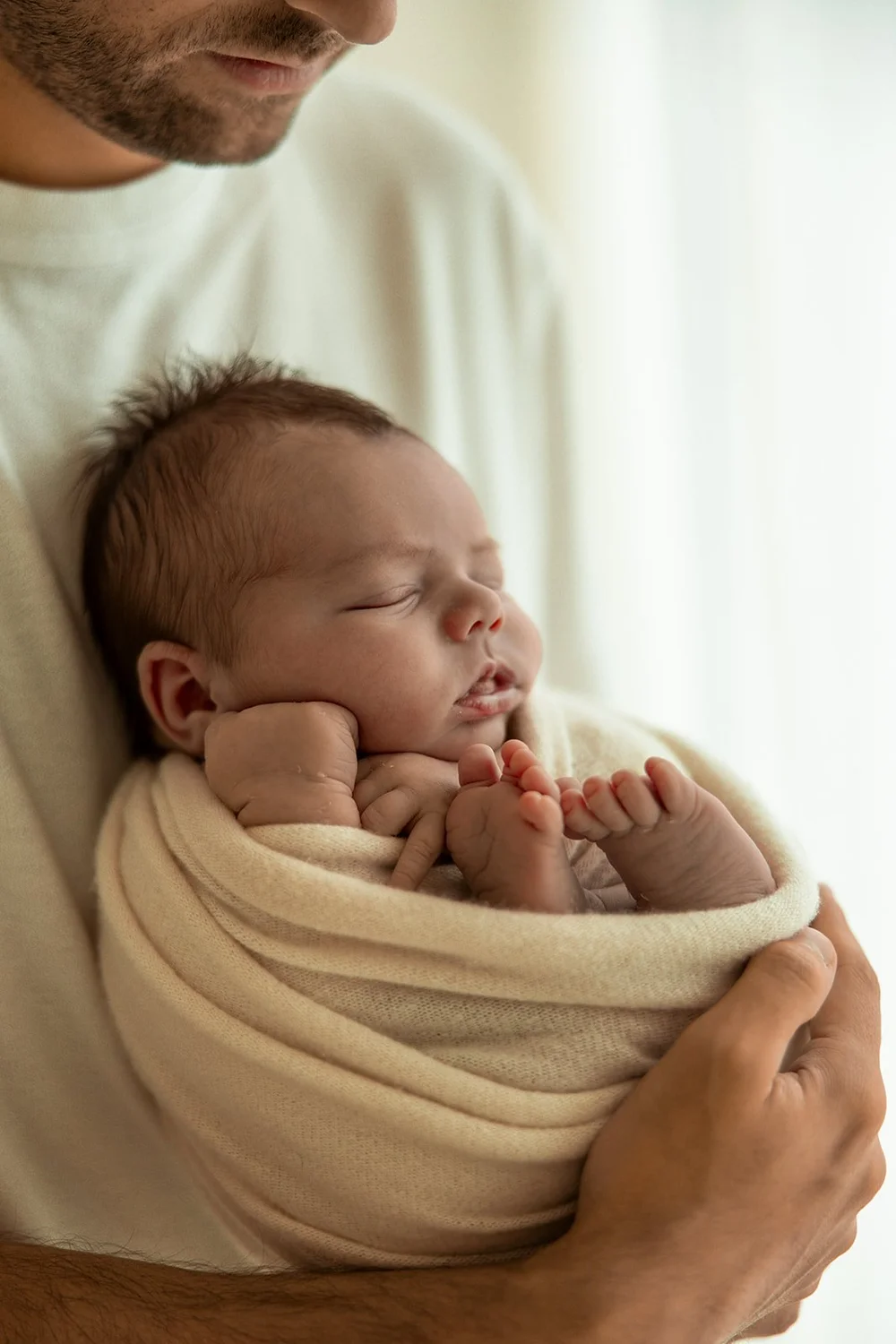 Slapende newborn in een doek in papa's handen