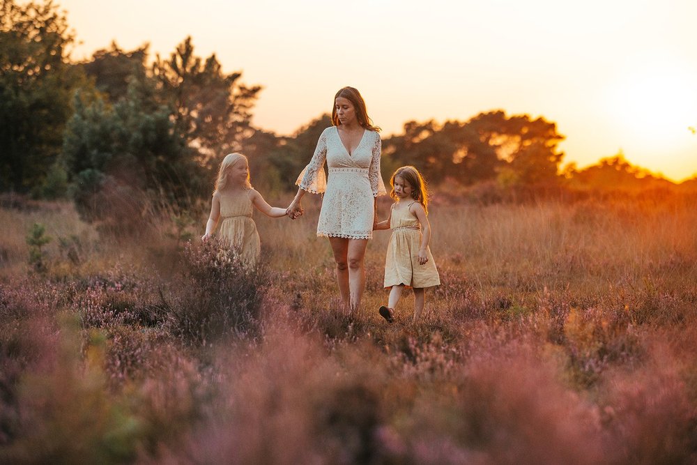 Mama wandelt met haar dochters door de heide bij zonsondergang