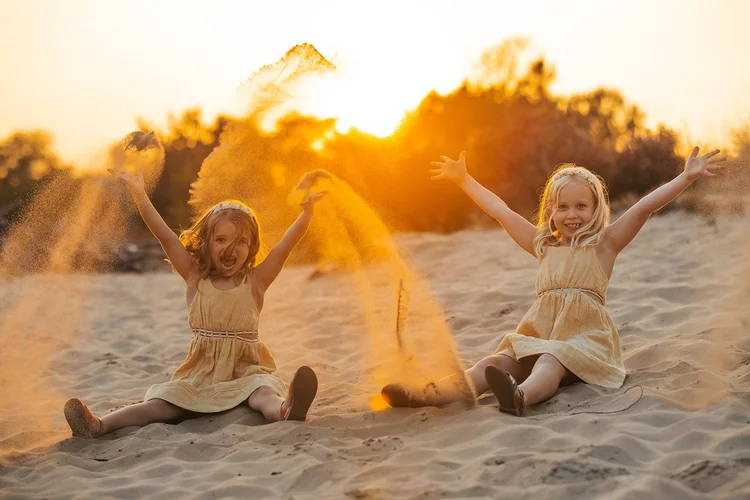 Kinderen springen in het zand bij zonsondergang
